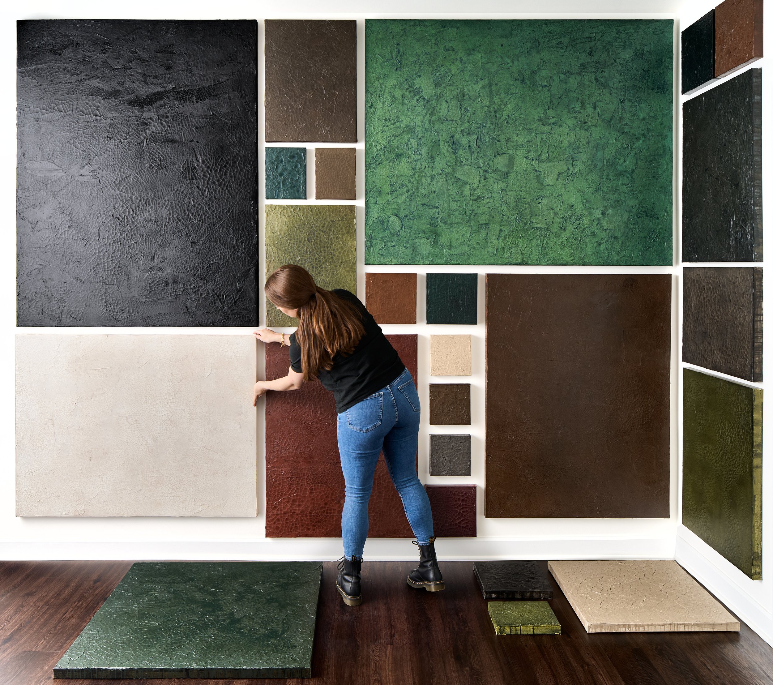 DC area abstract artist adjusts original textured paintings on canvas on art studio gallery wall, with various colored textured tile samples displayed.