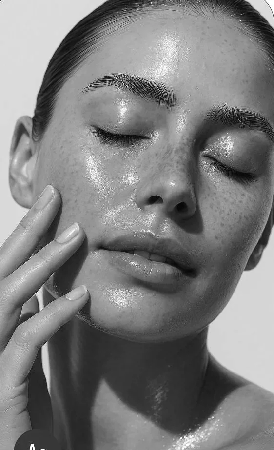 A black and white close-up photo of a woman with her eyes closed and her head tilted slightly upward, showing smooth skin and dark hair slicked back.