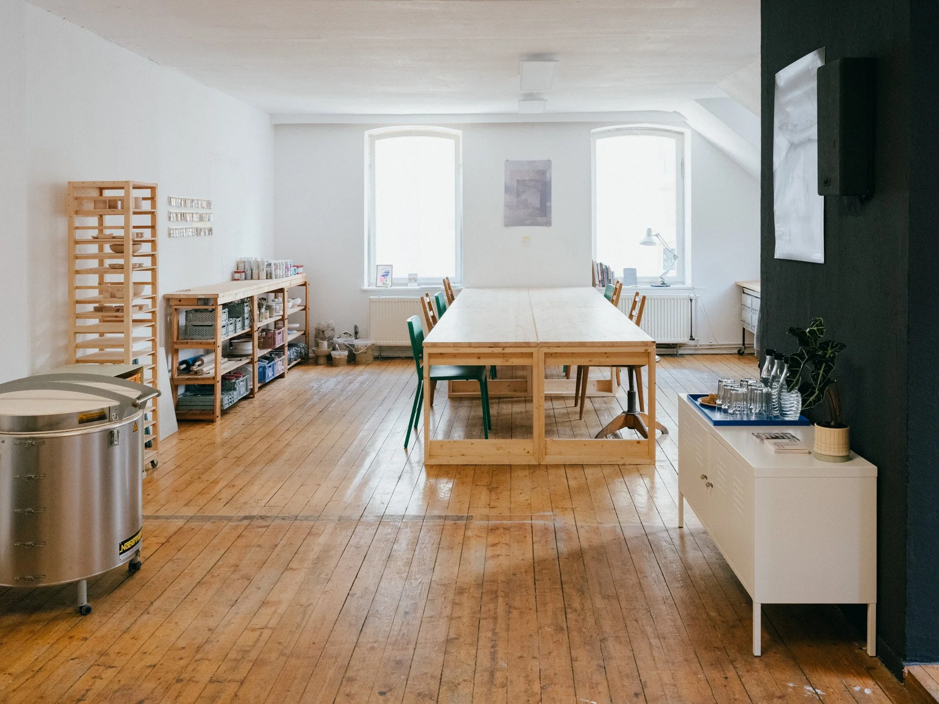 Foto vom Atelier, es ist ein großer Arbeitstisch, Regale und ein Brennofen zu sehen.