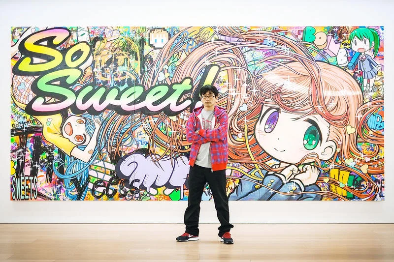 MR., aqui na frente de uma de suas obras, trabalha com a estética exagerada da cultura otaku - fonte da foto é o Hypebeast