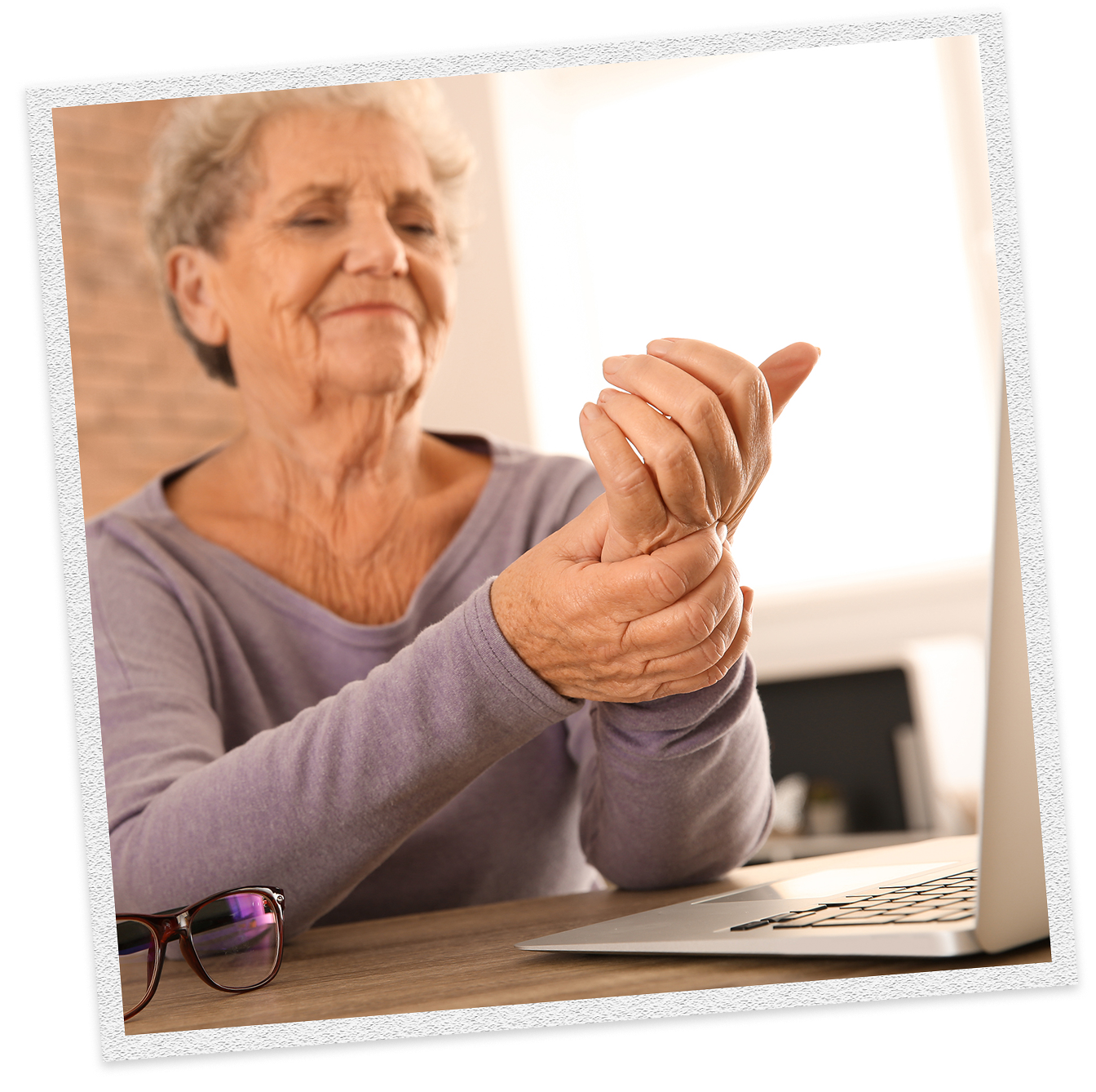An elderly woman with arthritis rubs her wrist in front of a laptop. CBD may be helpful for pain and inflammation.