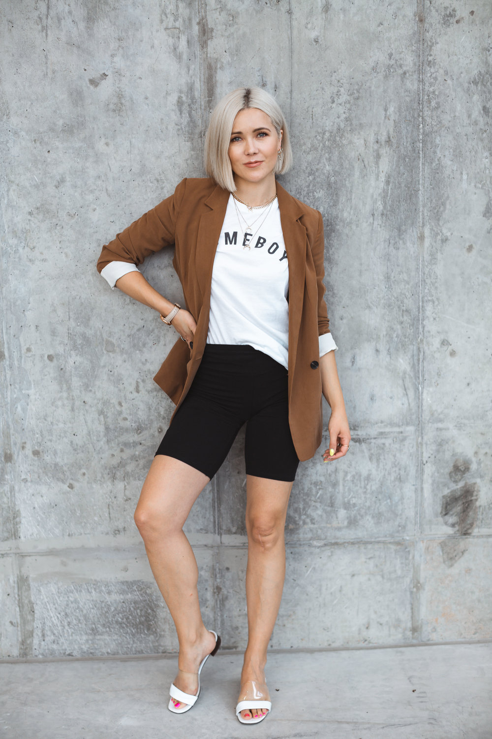 Copy of blonde woman in a brown blazer leaning against a concrete wall
