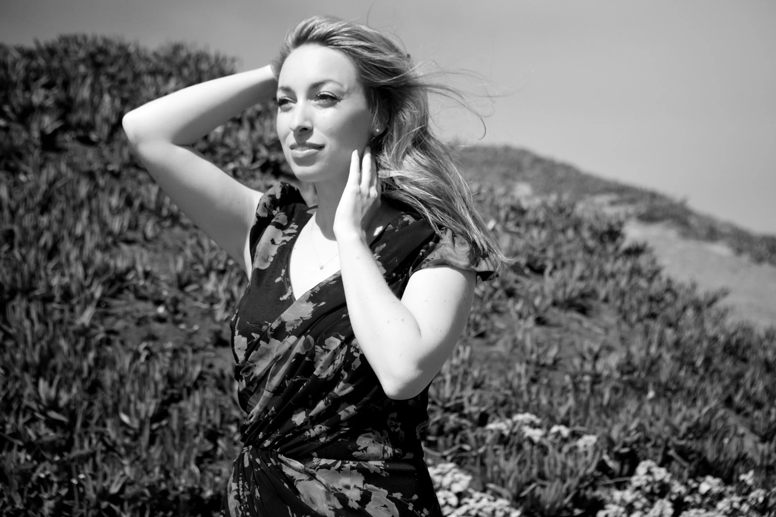 Black-and-white headshot by Kersh Branz featuring Leslie wearing floral dress, outside.