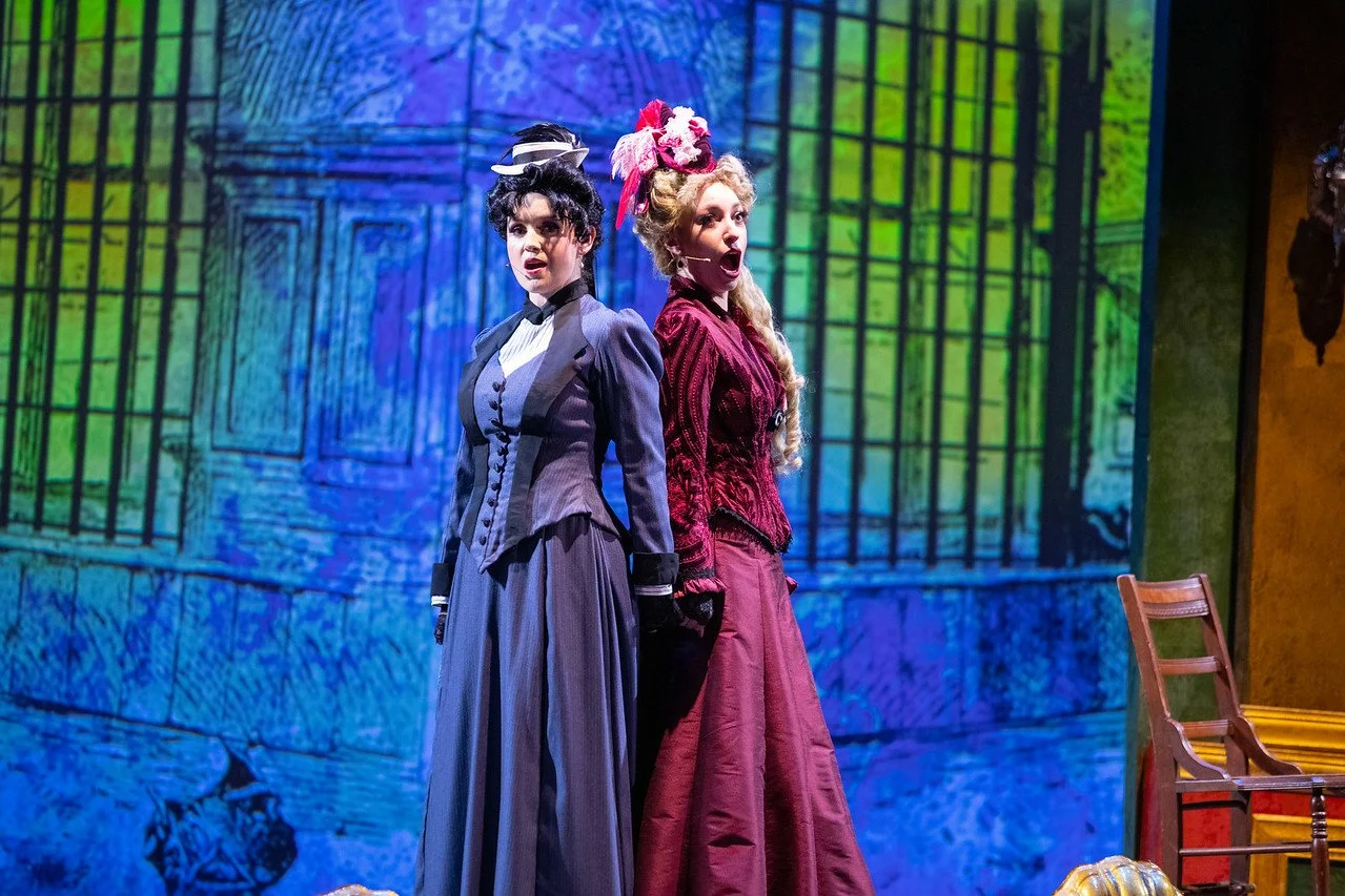  Leslie as Sibella Hallward, wearing burgundy dress and blond wig, in  A Gentleman’s Guide to Love and Murder  with Lamplighters Music Theatre, pictured with castmate. Photo by Joe Giammarco. 