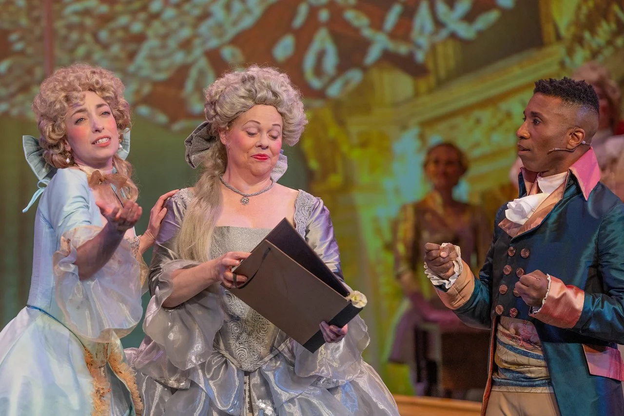  Leslie as Lady Lilette Sauvoirfaire, wearing a blue dress and blond wig, in  By Georges!  with Lamplighters Music Theatre, pictured with castmates. Photo by Joe Giammarco. 