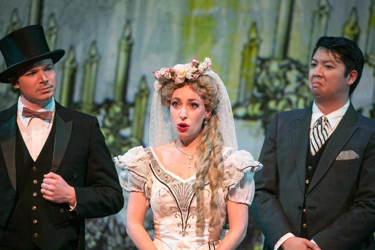  Leslie as Sibella Hallward ,  wearing white wedding dress and blond wig, in  A Gentleman’s Guide to Love and Murder with Lamplighters Music Theatre, pictured with castmates. Photo by Lucas Buxman. 