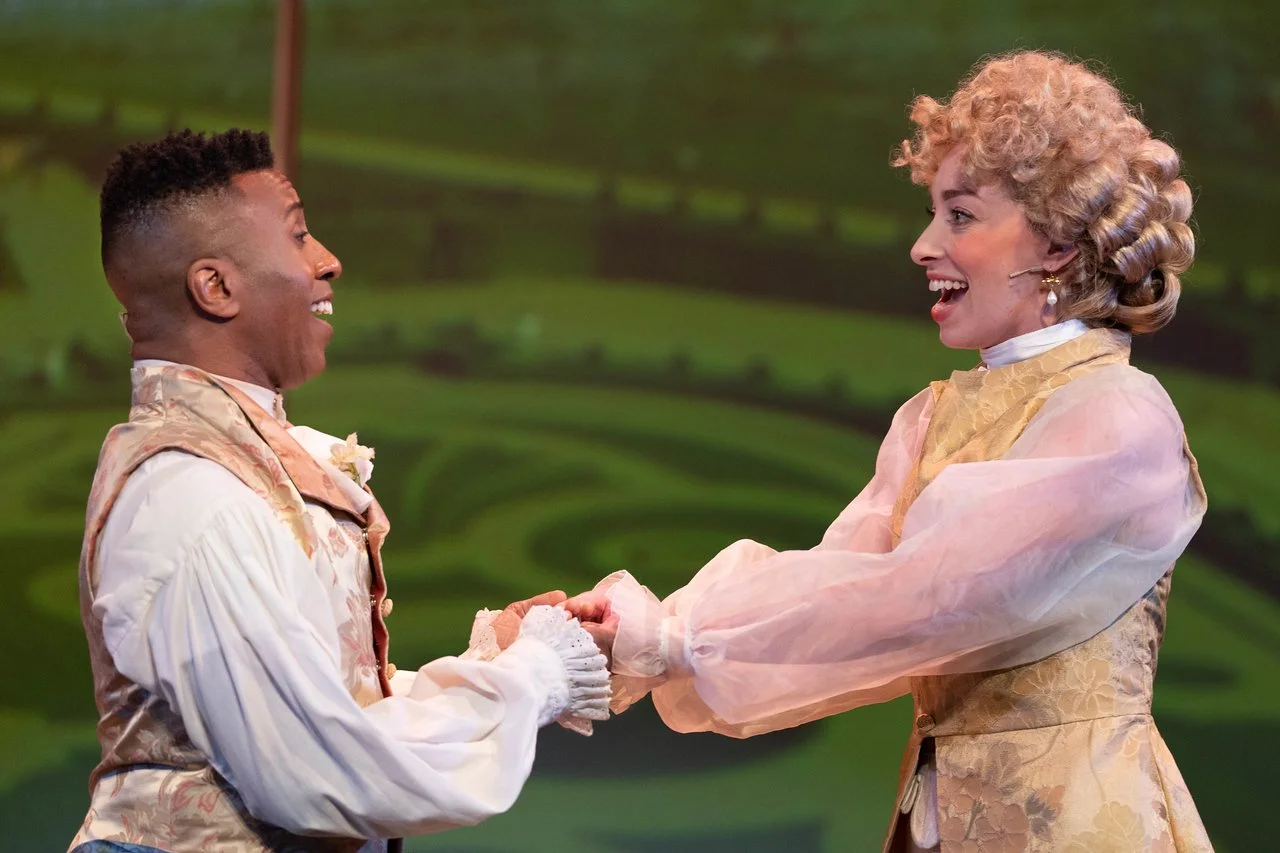  Leslie as Lady Lilette Sauvoirfaire, wearing white pants, gold vest, and blond wig, in  By Georges!  with Lamplighters Music Theatre, pictured with castmate. Photo by Joe Giammarco. 