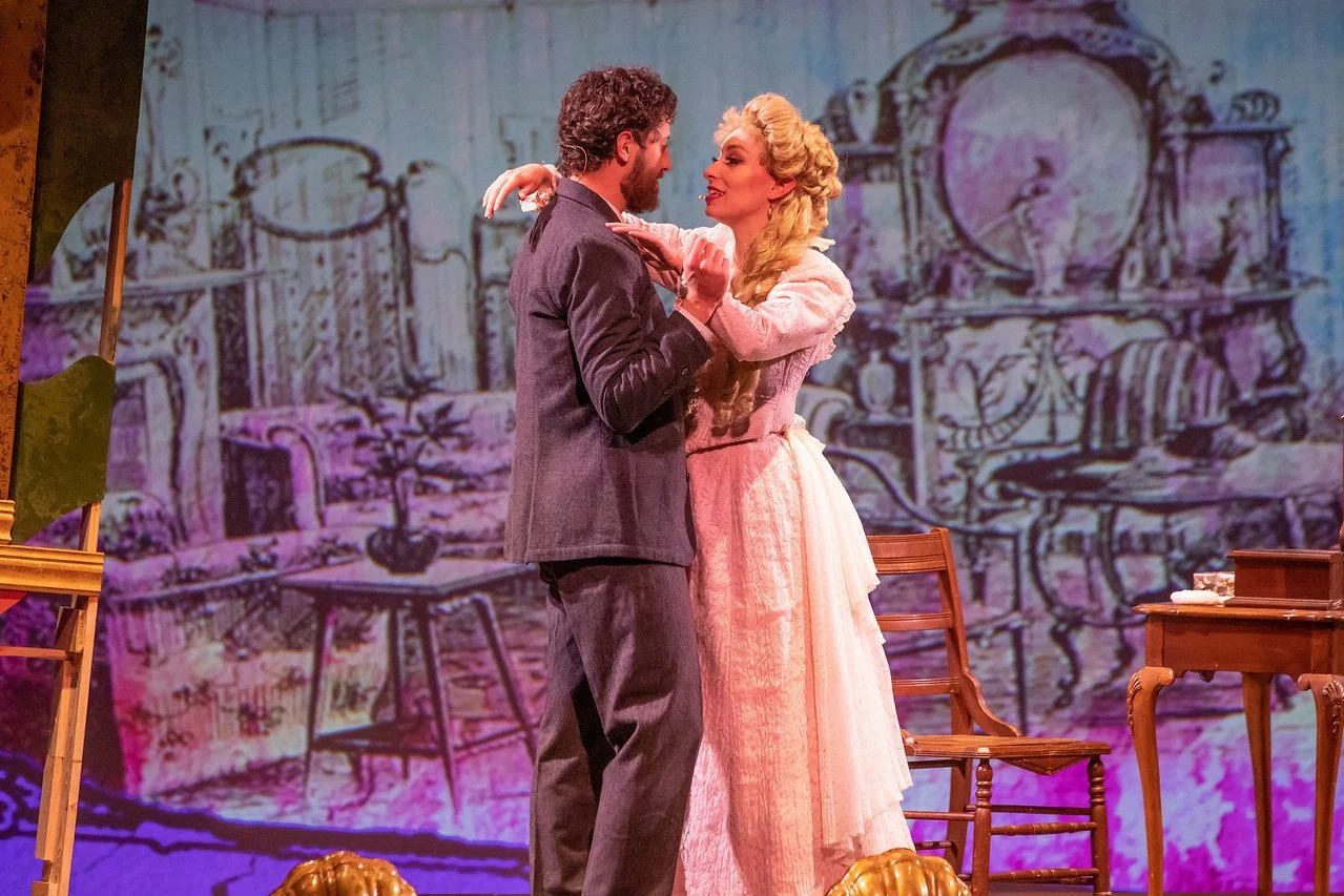  Leslie as Sibella Hallward, wearing pink dress and blond wig, in  A Gentleman’s Guide to Love and Murder  with Lamplighters Music Theatre, pictured with castmate. Photo by Joe Giammarco. 