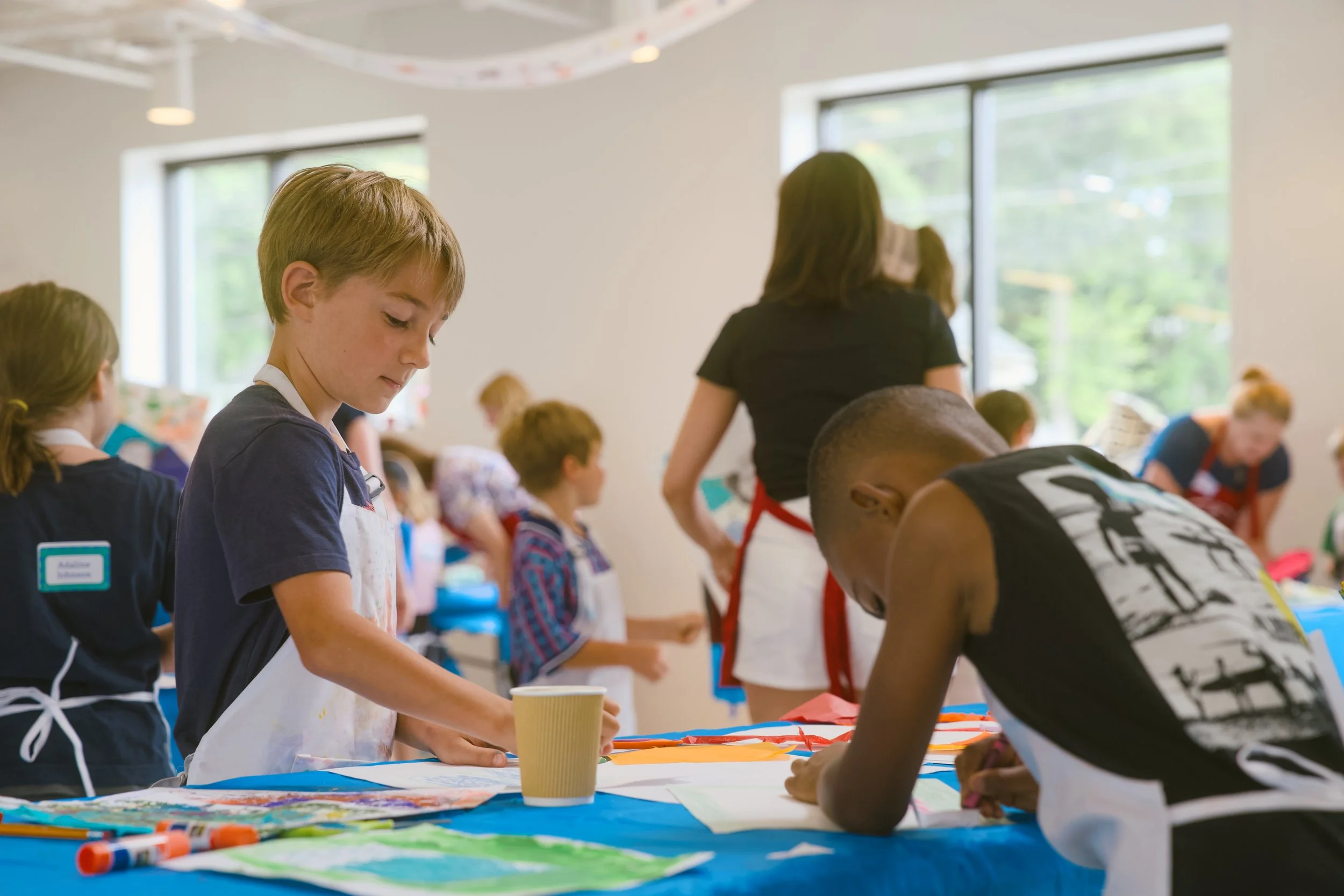 Children participating in an arts and crafts activity in a classroom, engaging in painting and crafting on a table covered with art supplies.