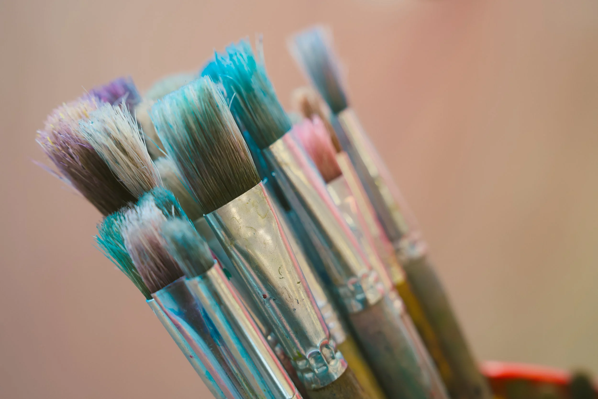 Close-up of paintbrushes with colorful bristles arranged in a row against a blurred background.