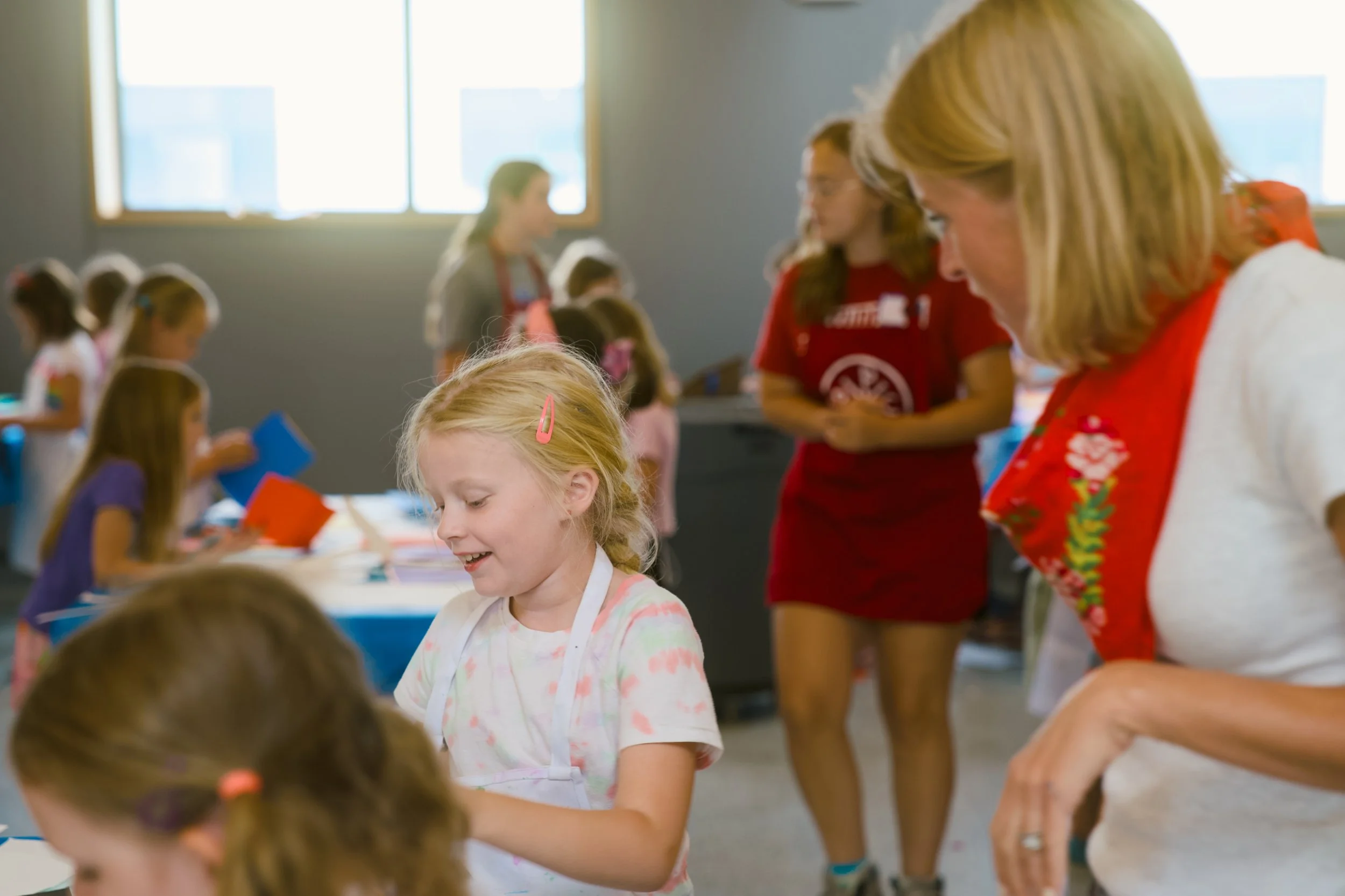Children participating in an arts and crafts activity in a classroom as adults assist them.