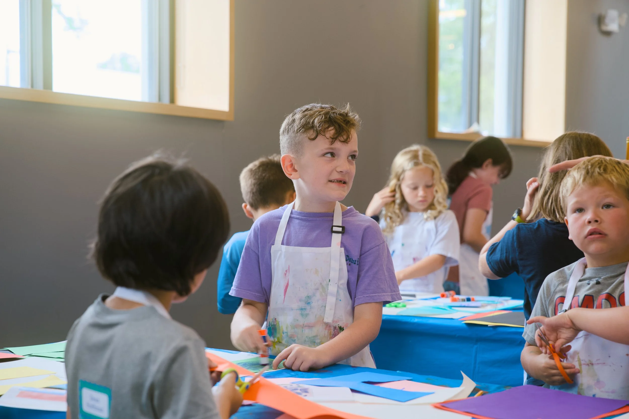 Young children participating in an arts and crafts activity in a classroom with large open windows.