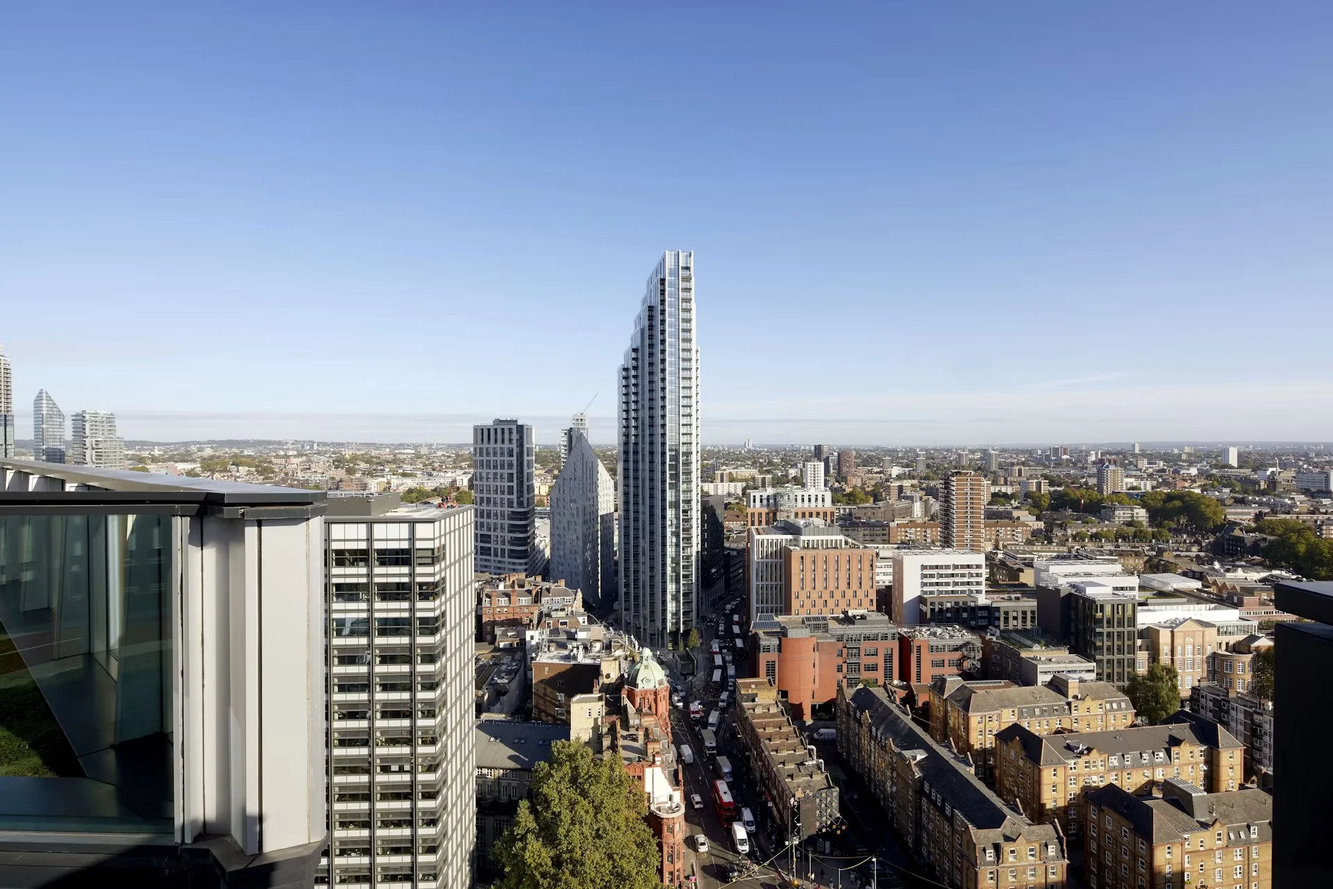 City skyline with modern high-rise buildings, some under construction, under a clear blue sky, including a mix of glass and concrete structures, with streets filled with cars and trees.