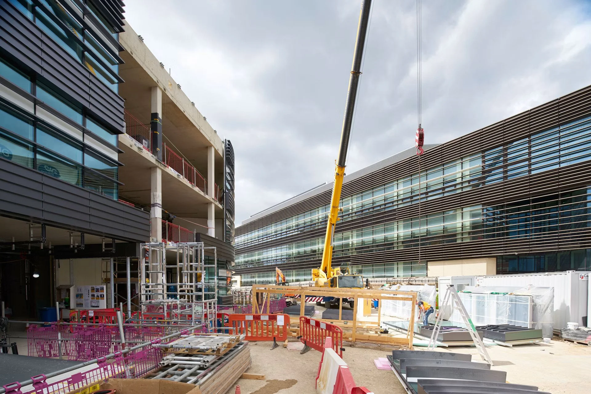 Construction site with scaffolding, a crane, and two modern buildings under construction against a cloudy sky.