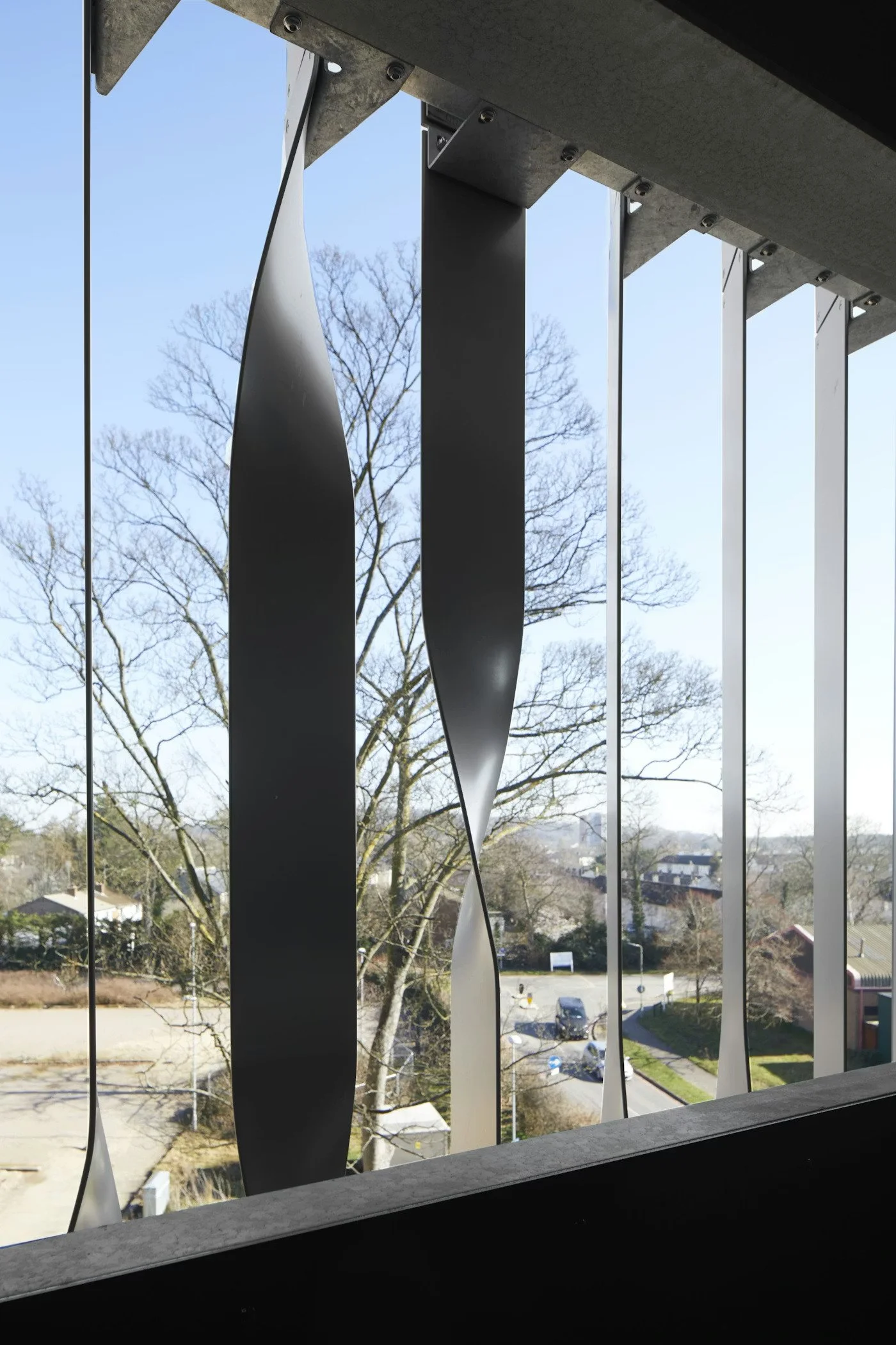 View through window with metal bars showing trees, houses, and a parking lot outside on a clear day.