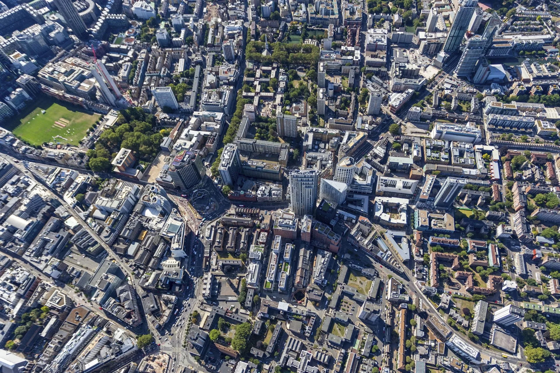 An aerial view of a dense urban area with multiple tall buildings, streets, and a large green park in the center.