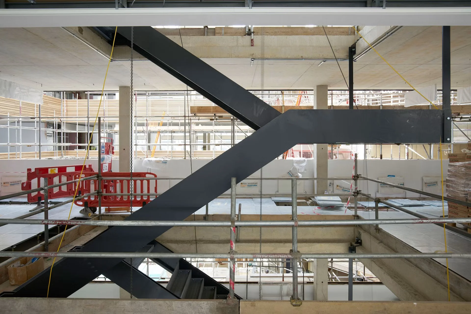 Interior of a building under construction with scaffolding, a staircase, and safety fencing.