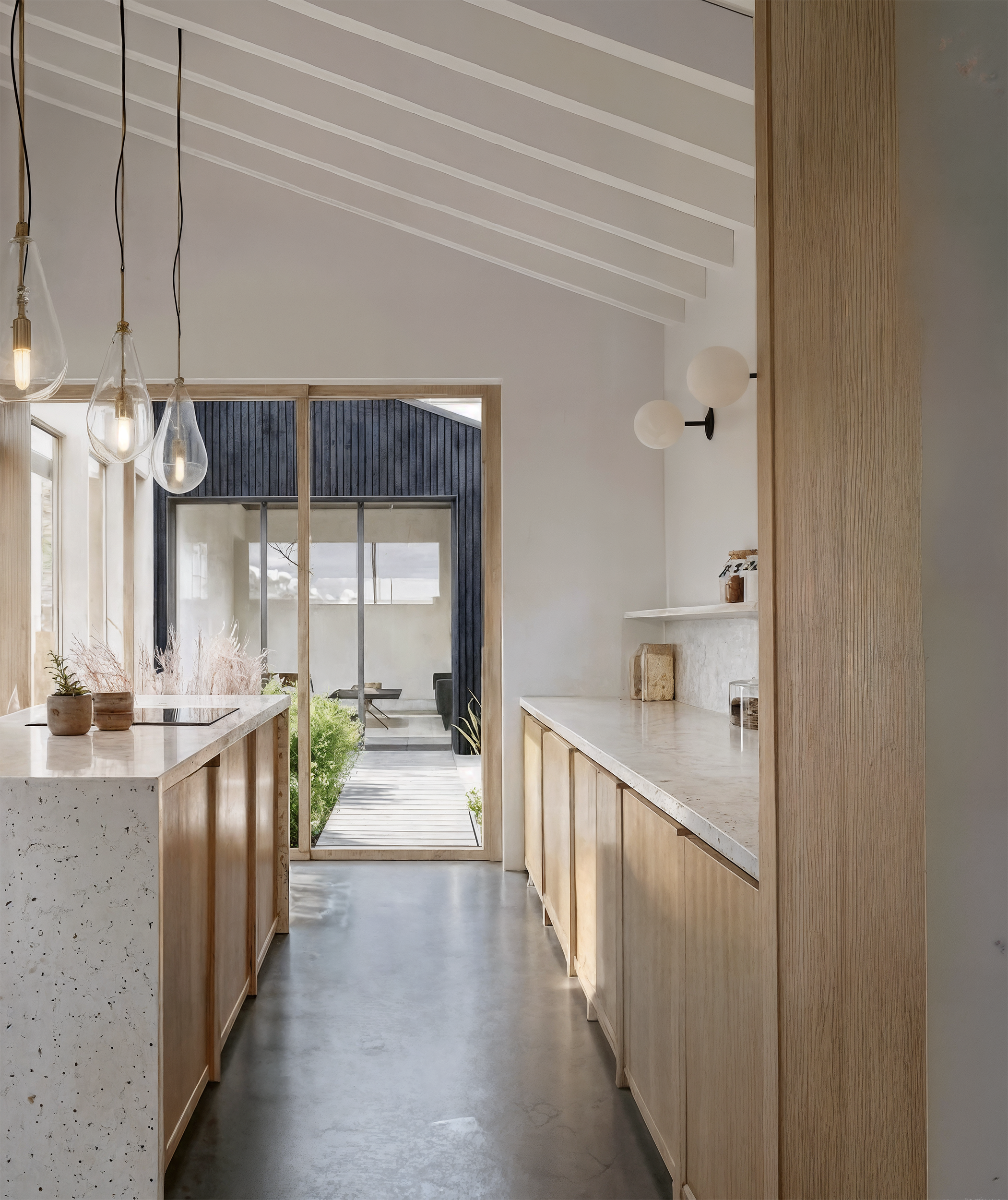 Modern kitchen with wooden cabinets, marble countertops, hanging pendant lights, and a sliding glass door leading outside.