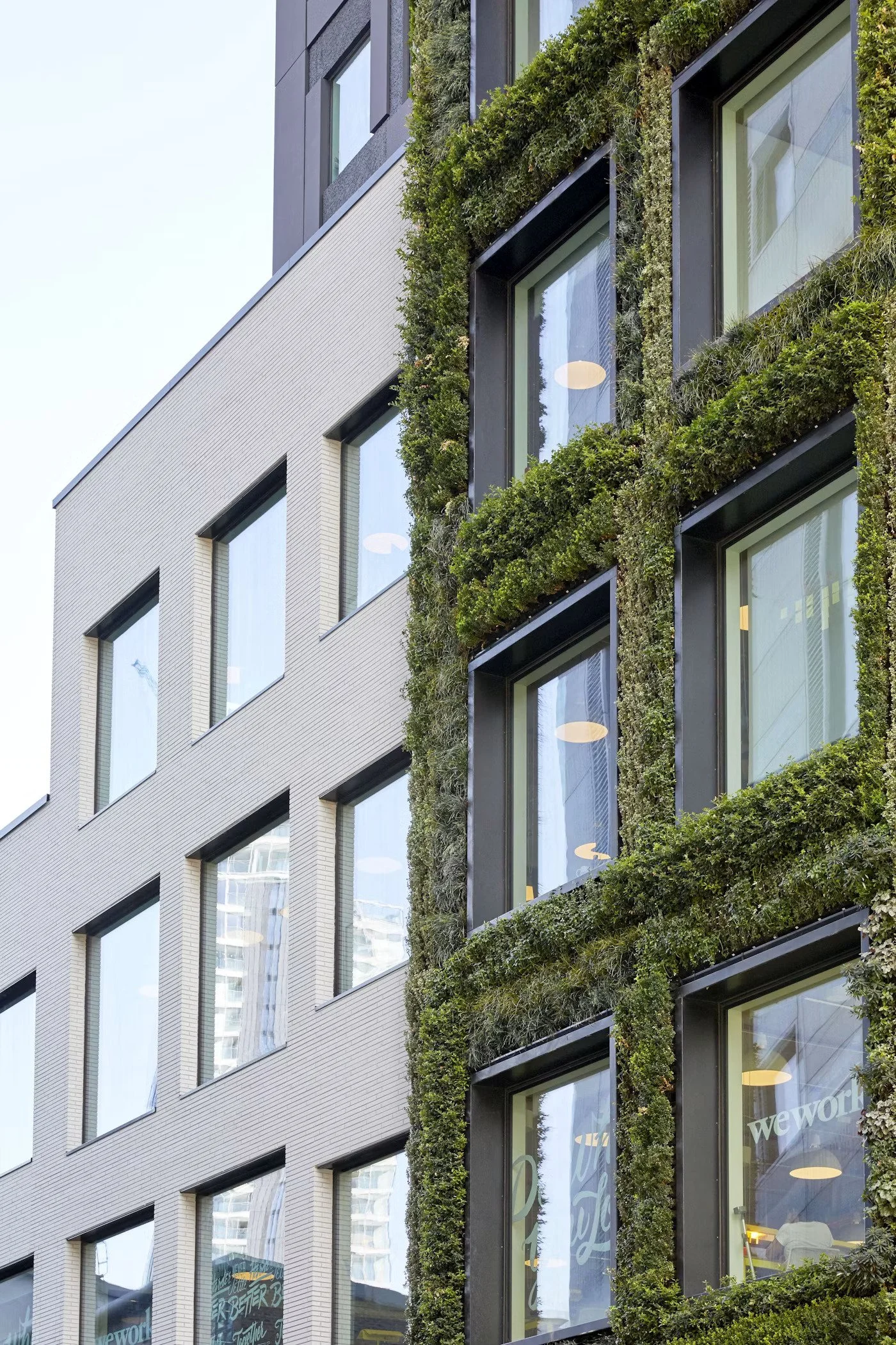 A modern building with large glass windows and a vertical garden with lush green plants growing around the windows.