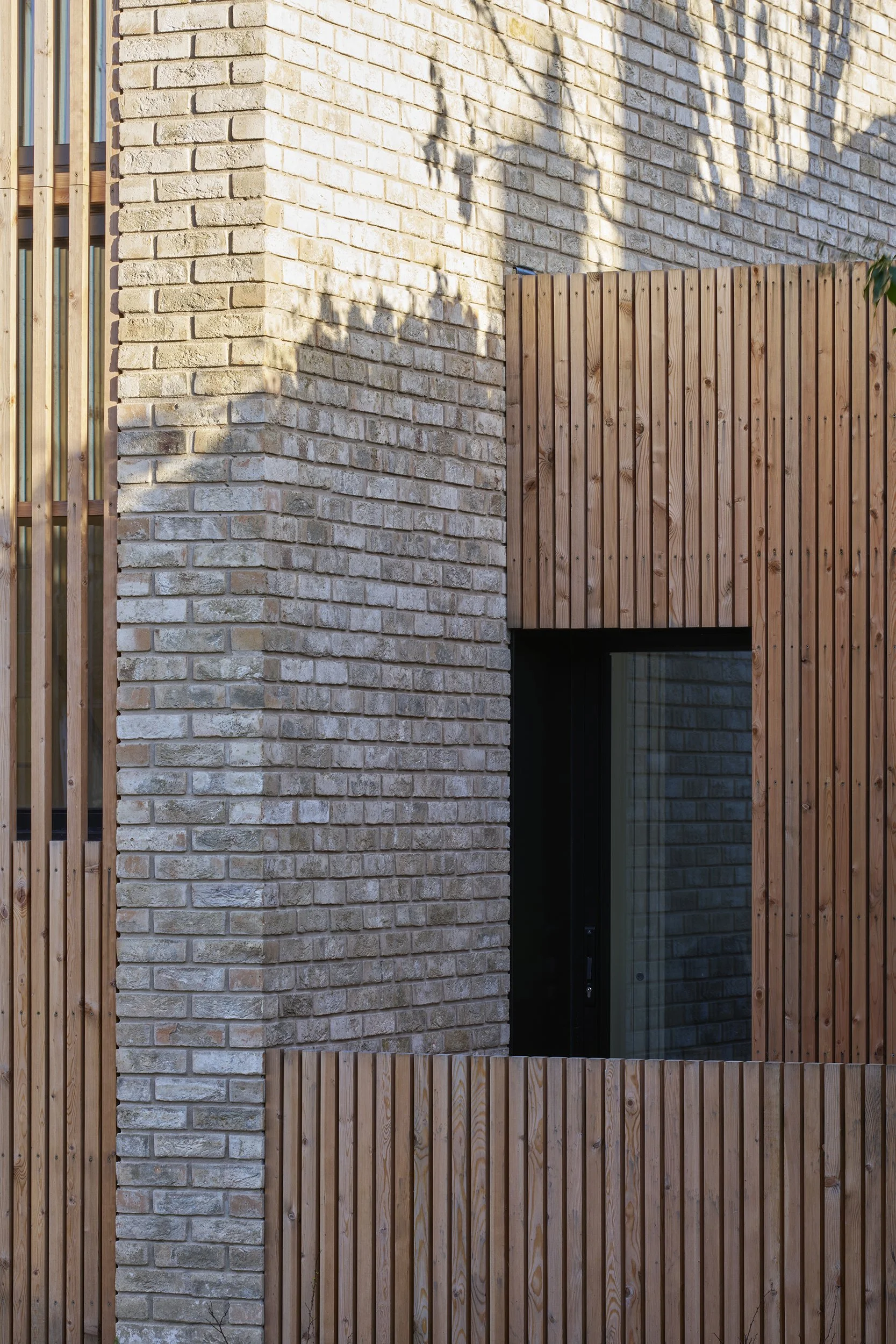 Close-up of a modern building's exterior wall combining brick and wooden paneling, with a window partially visible.