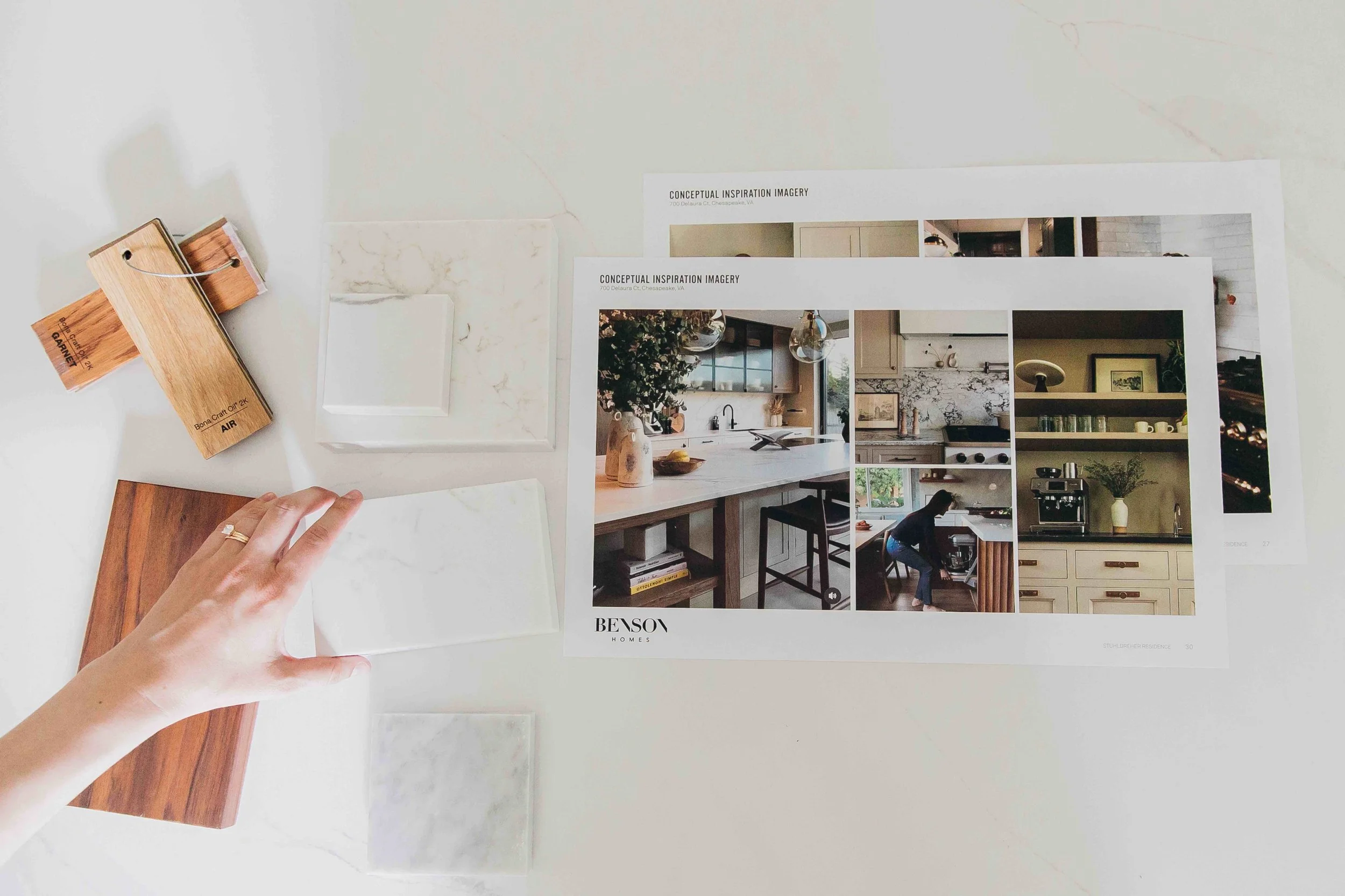 Hand reaching for marble sample on table next to other samples of marble and wood and printed photo inspiration for kitchen design