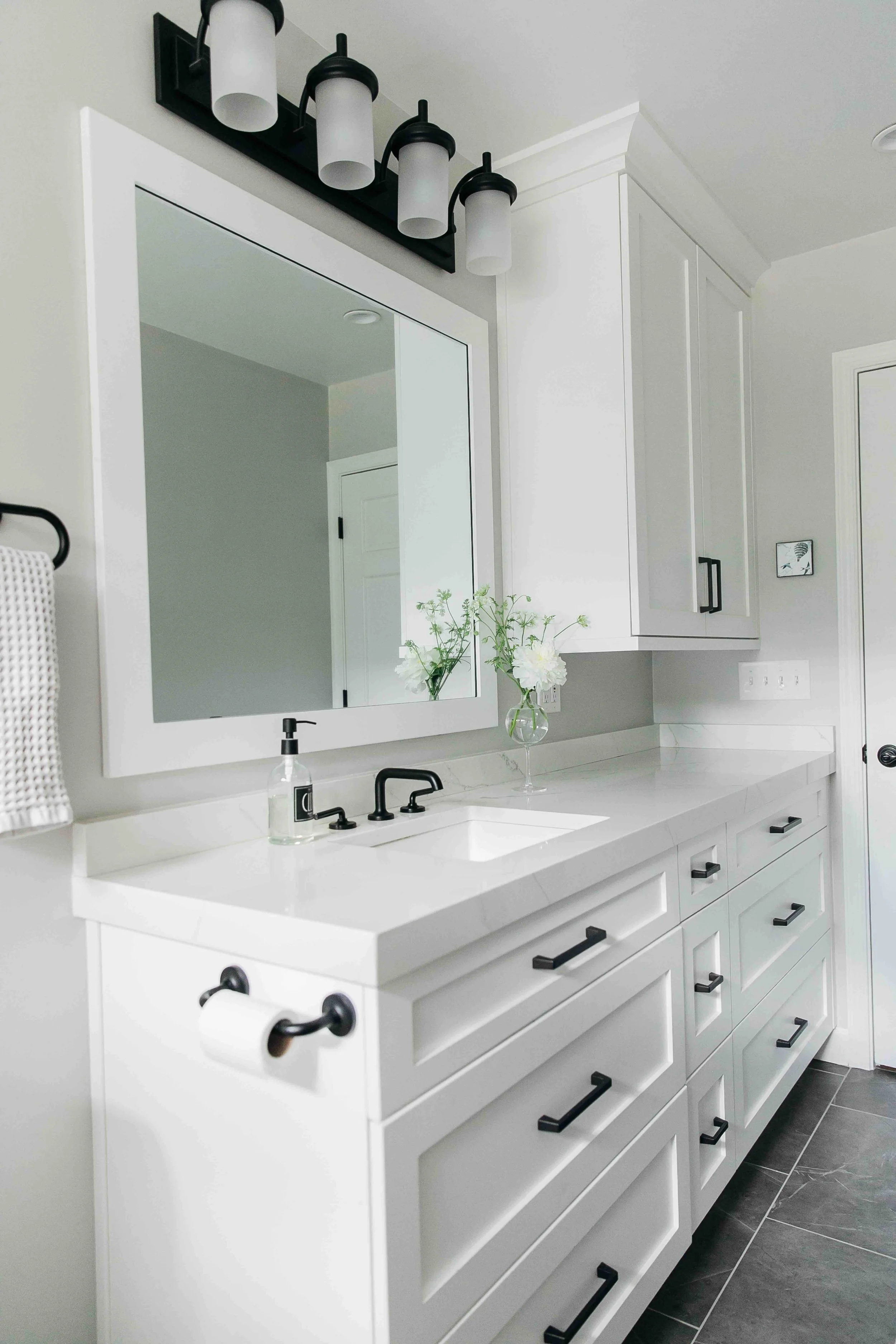 Guest bathroom with large counter space, white cabinets, marble counter and black accents