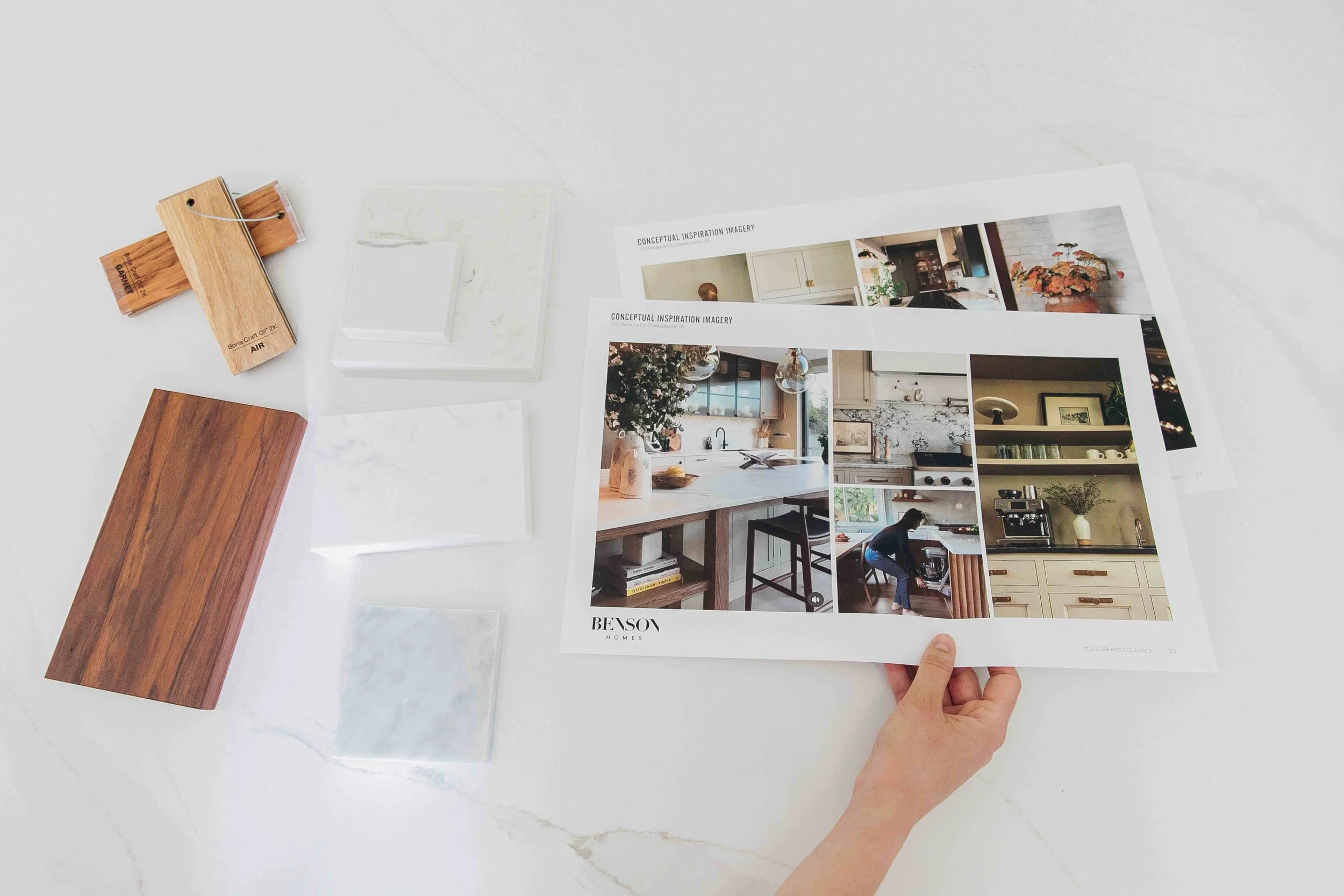 Samples of tile and wood next to printed out inspiration imagery for a modern kitchen with a hand reaching for the paper of imagery