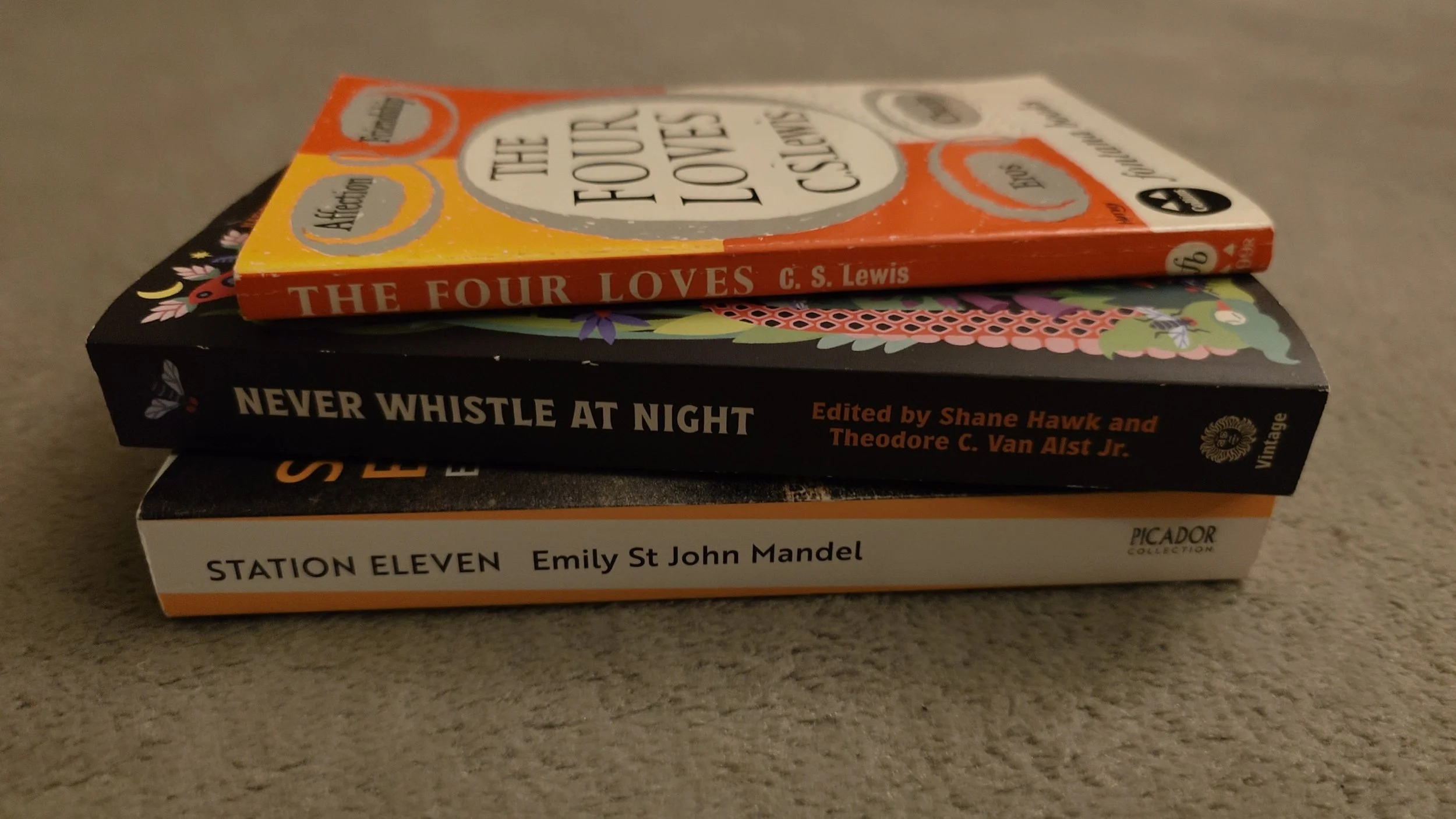 A stack of paperback copies of the books listed below, sitting on a rather worn-out grey carpet
