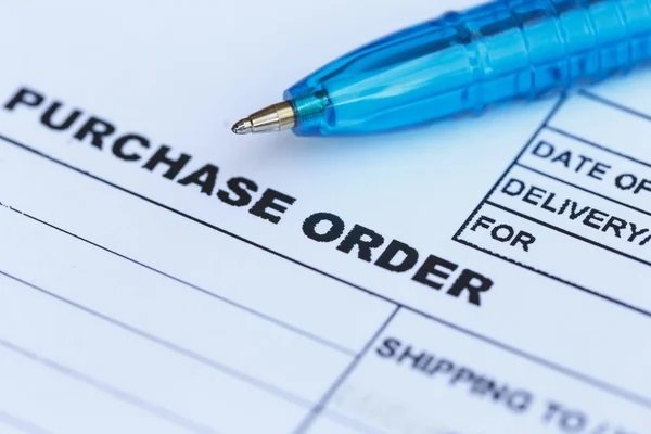 A purchase order form with a blue pen resting on top, showing fields for date, delivery, and shipping details.