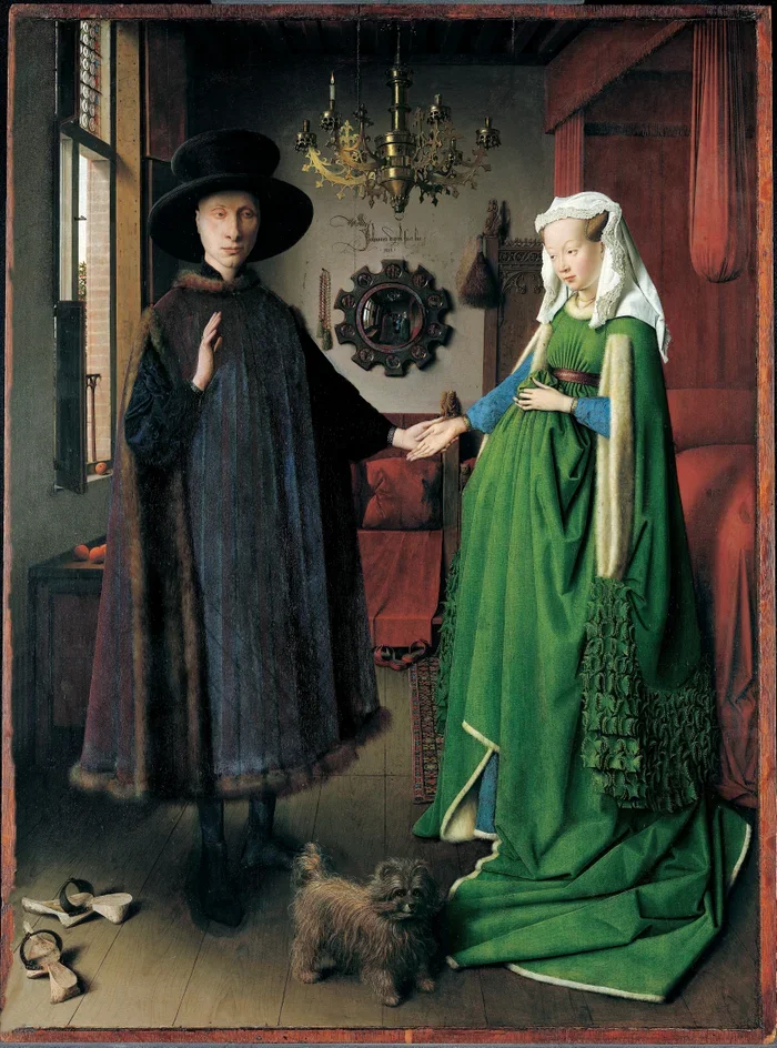 A woman with pale skin, dressed in dark clothing and a large black hat, holds hands with a woman wearing a green and blue gown with a white head covering. They stand in a room with a chandelier, a mirror, and a red curtain. A small fluffy dog is on the wooden floor in front of them.