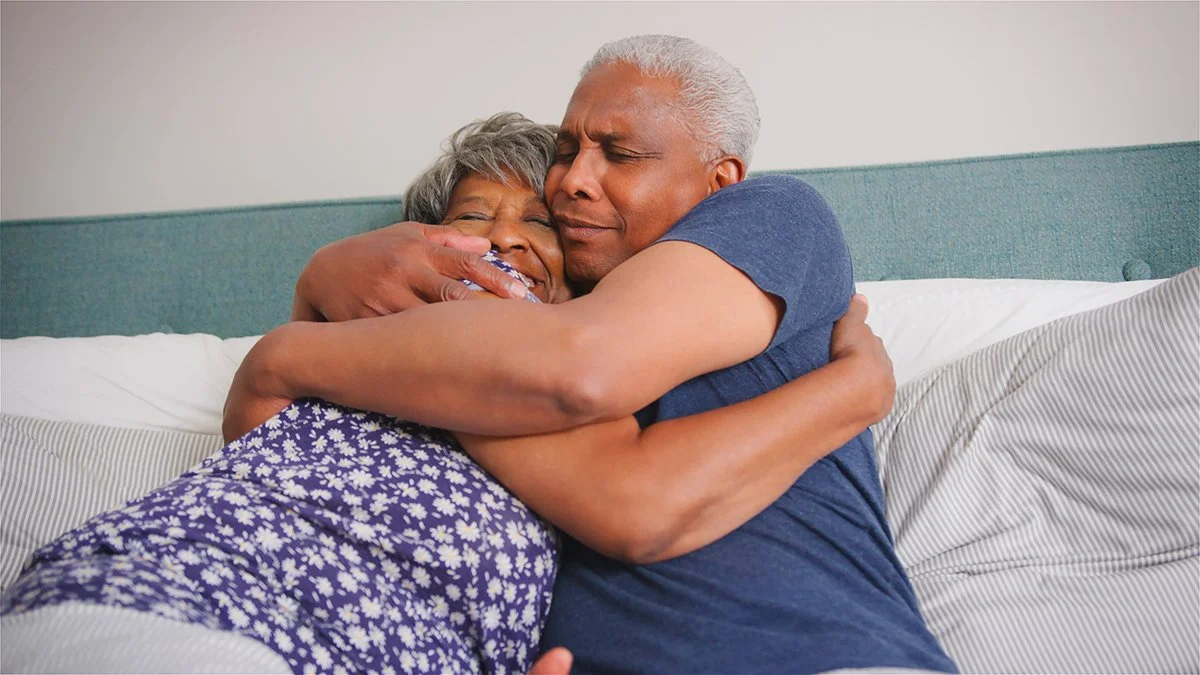 Loving Senior Couple At Home Cuddling In Bed In Morning