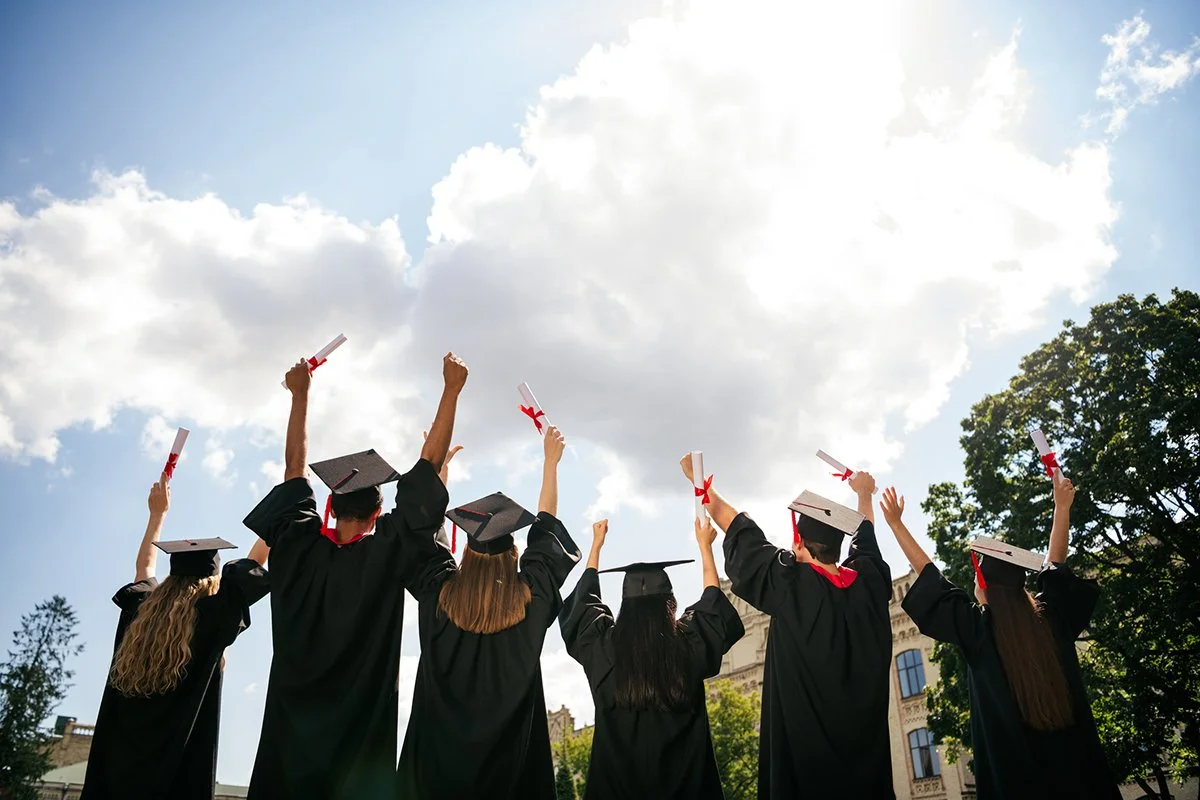 group of college students in cap and gown, raise fists holding their diploma.