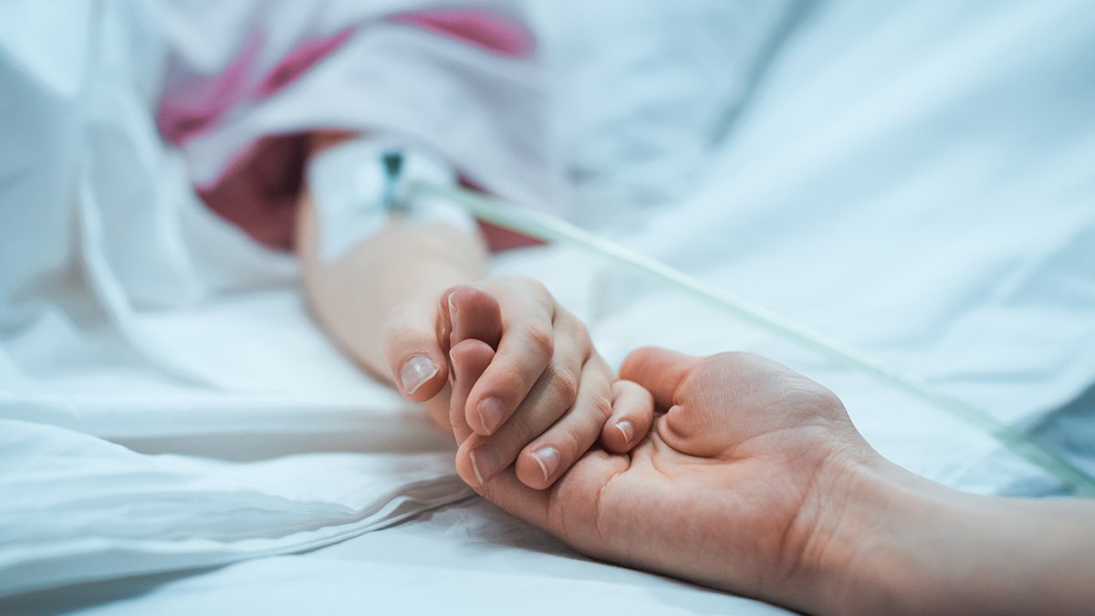 Close up image of holding hands in a hospital room. Person lying in the hospital bed is holding the hand of someone else who is there to comfort. ting.