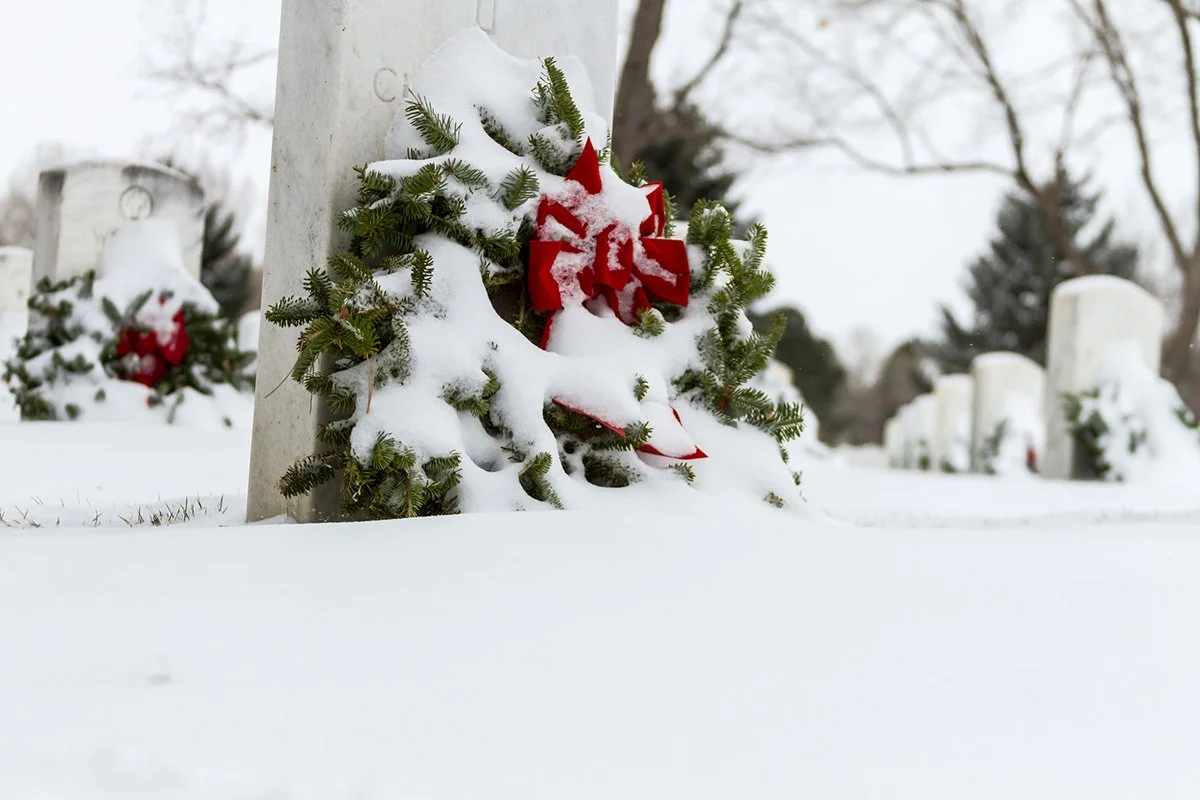 Close up of a Christmas wreath leaned up against a headstone in Arlington Cemetery, with more in the background.