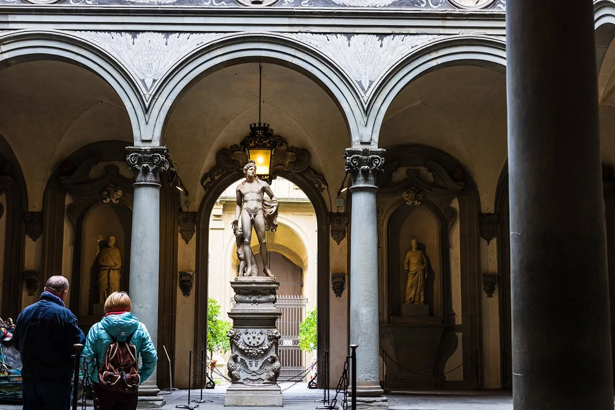 A couple of tourists in the foreground looking at David by Michelangelo in Galleria dell'Accademia in Florence, Italy