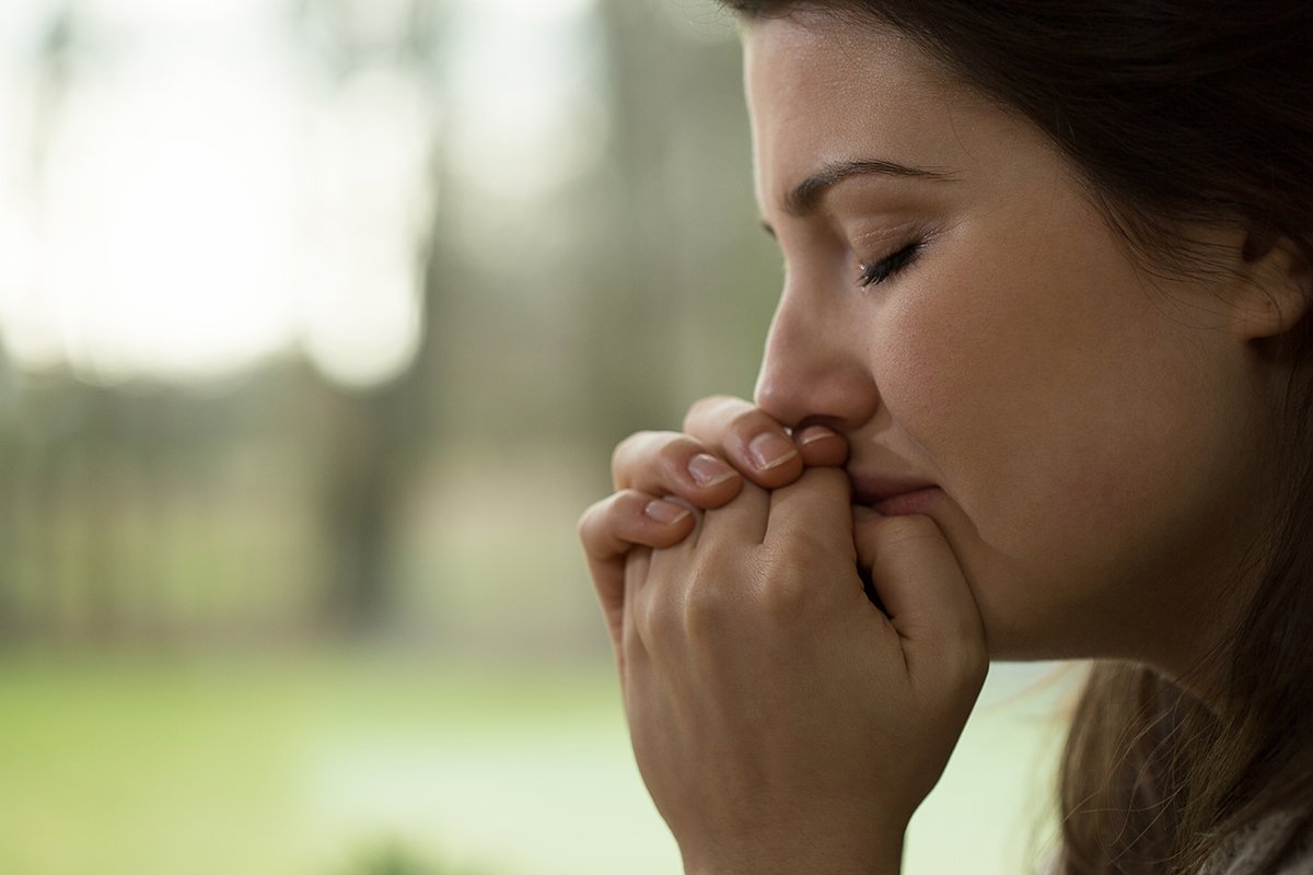 Close up of woman with eyes closes, clenched hand as if praying, and small tears coming from her eyes.