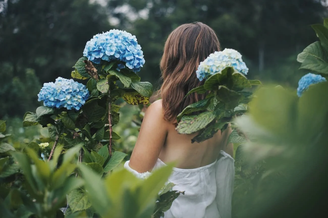 a woman outdoors in nature with blue flowers connects with feminine energy