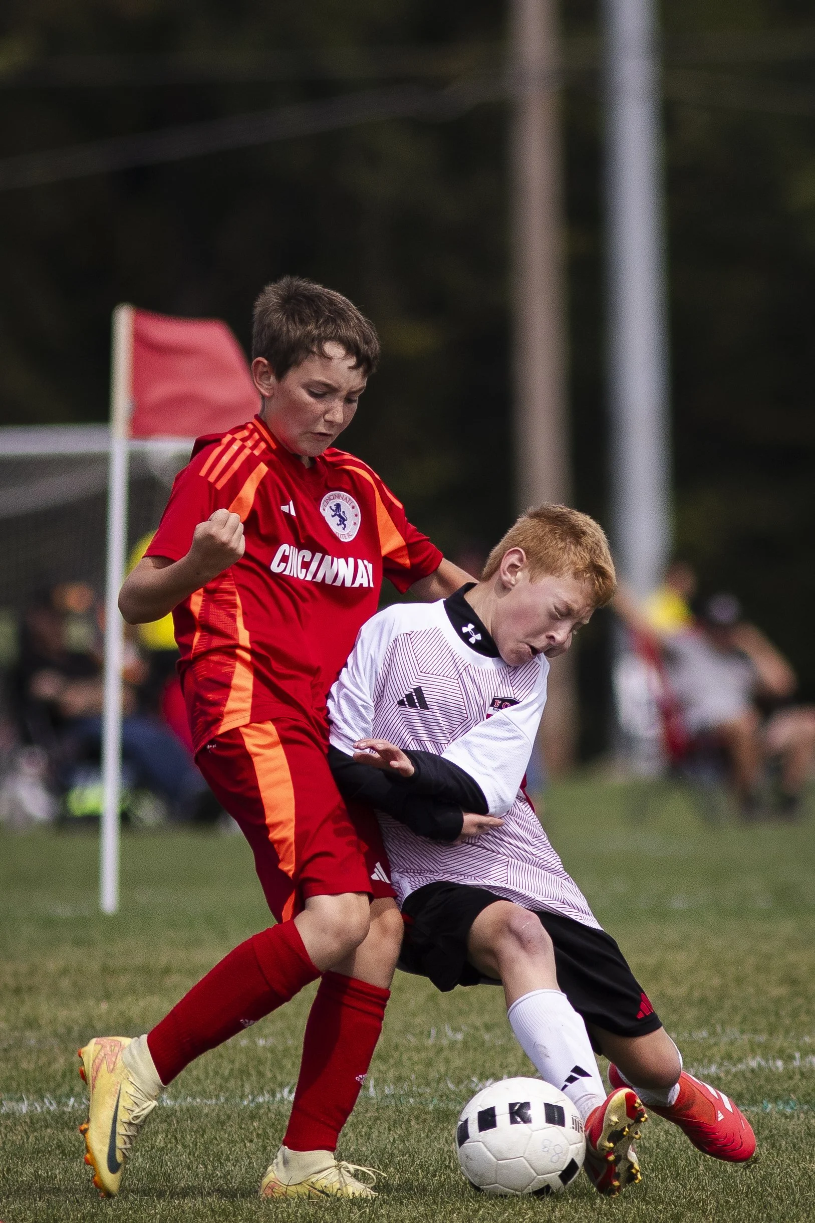 Two young boys playing soccer, one in a red uniform and the other in a white uniform, competing for the ball during a match on a grassy field.