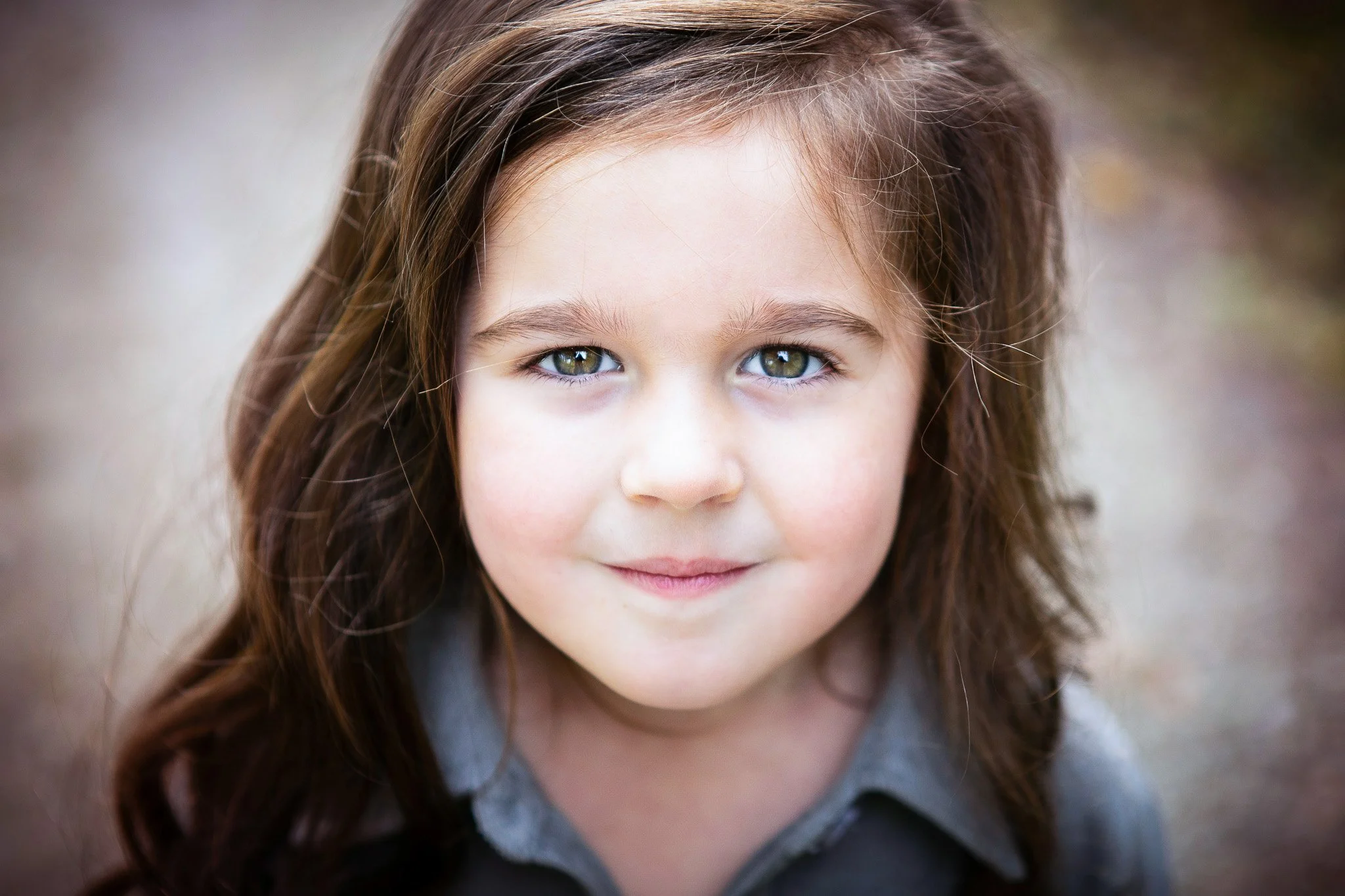 Close-up of a young girl with long brown hair and green eyes, outdoors.