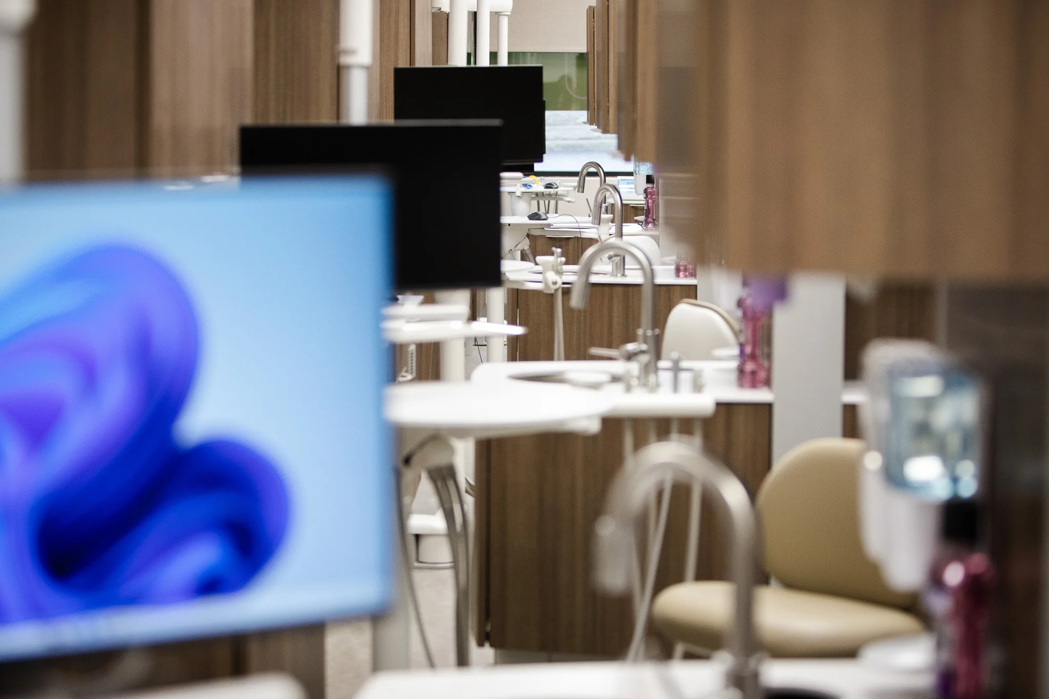 Multiple hospital or clinic sinks and mirrors arranged along a wall, with computer monitors and medical equipment nearby.