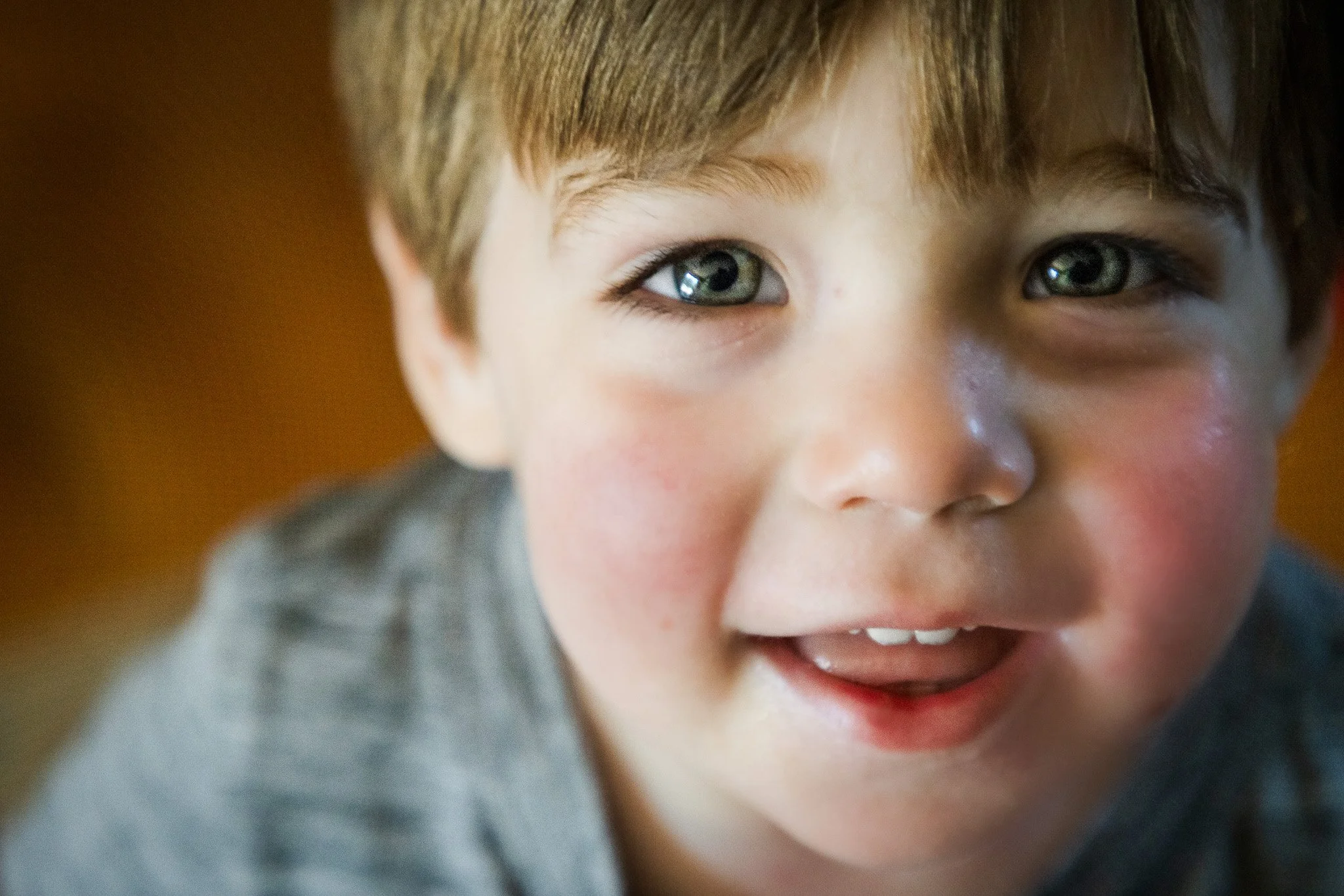 Close-up of a smiling young boy with brown hair and green eyes.