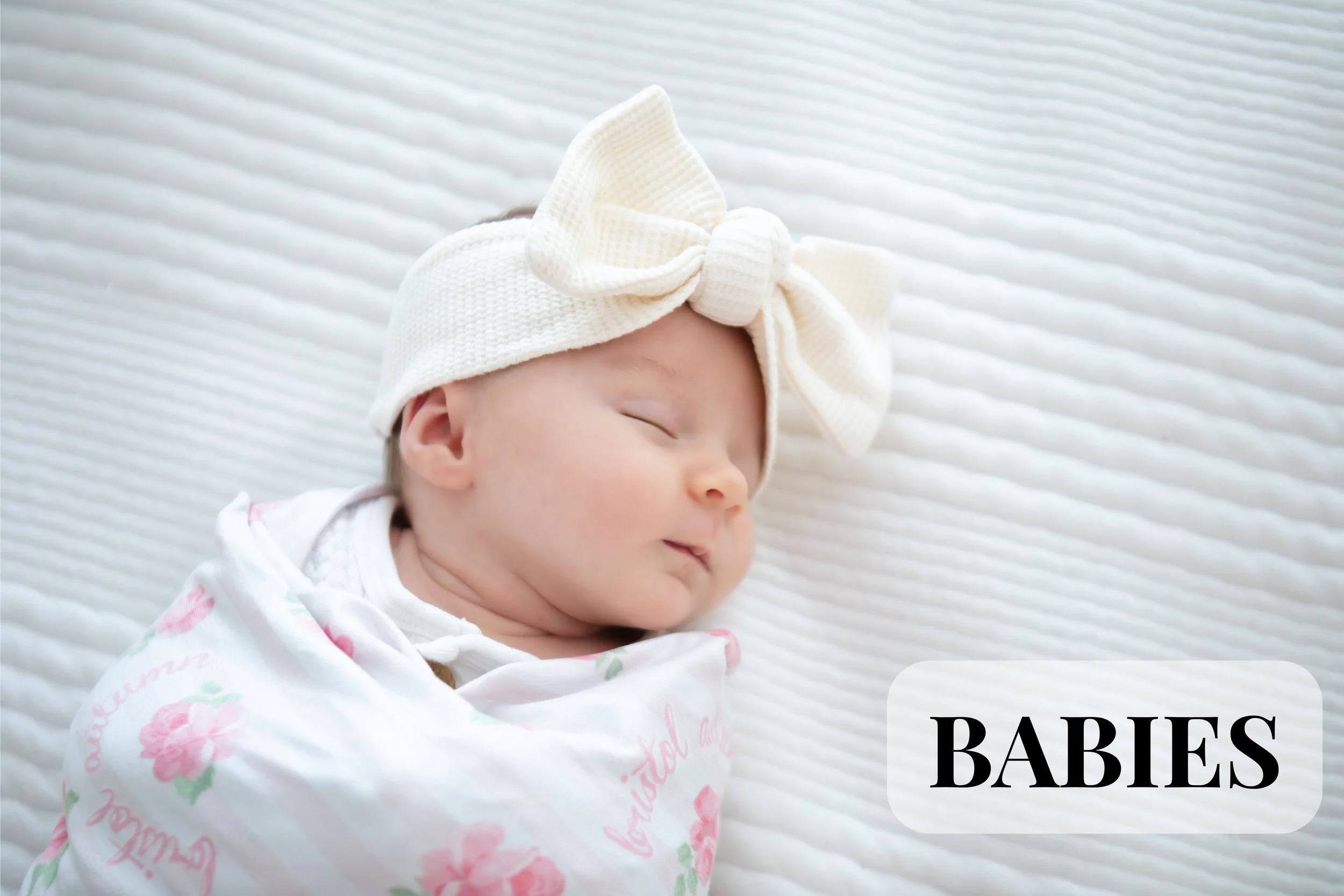 A newborn lifestyle session in Milford, Ohio. Profile of a sleeping baby girl with a bow headband, lying on a striped white blanket, wearing a floral pajama. The image includes the text "BABIES" in the bottom right corner.