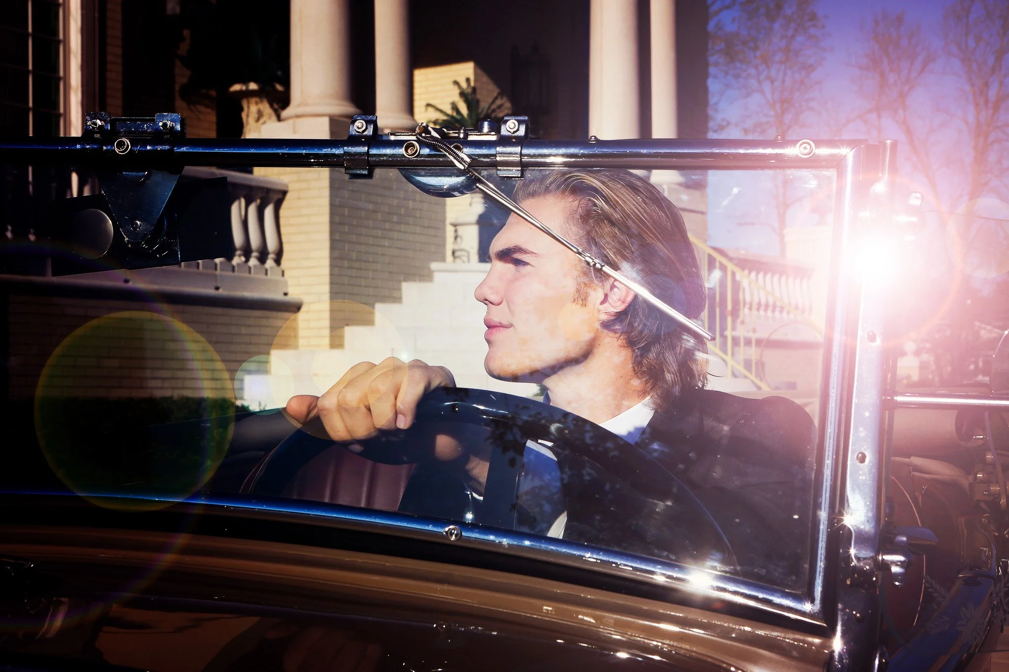 A man with long hair driving a vintage car on sunny day.