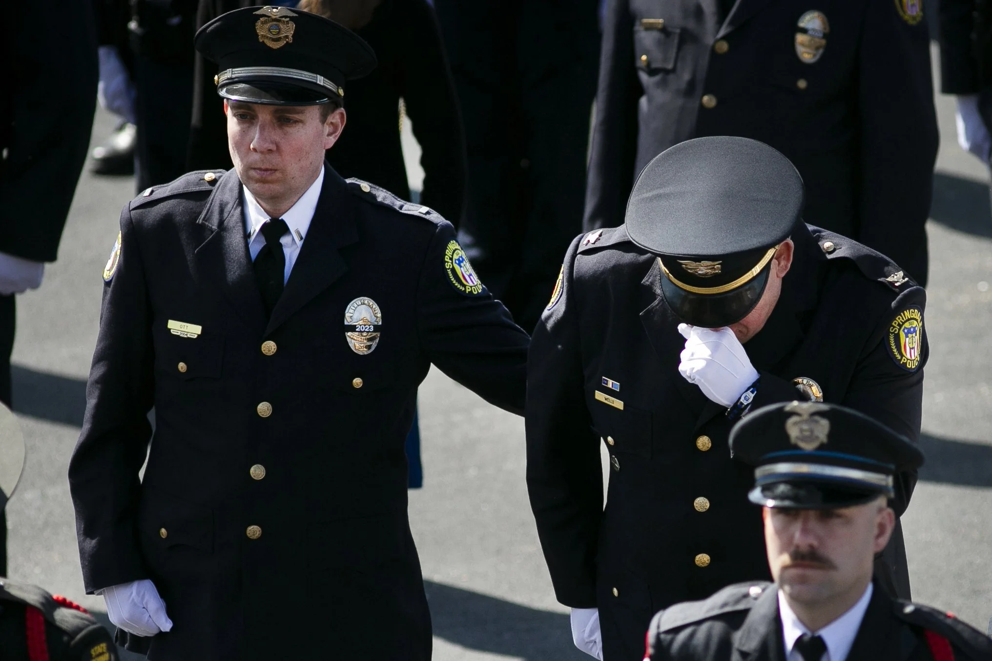 A group of police officers in uniform participating in a memorial or solemn ceremony. One officer appears to be crying, and others have serious expressions.