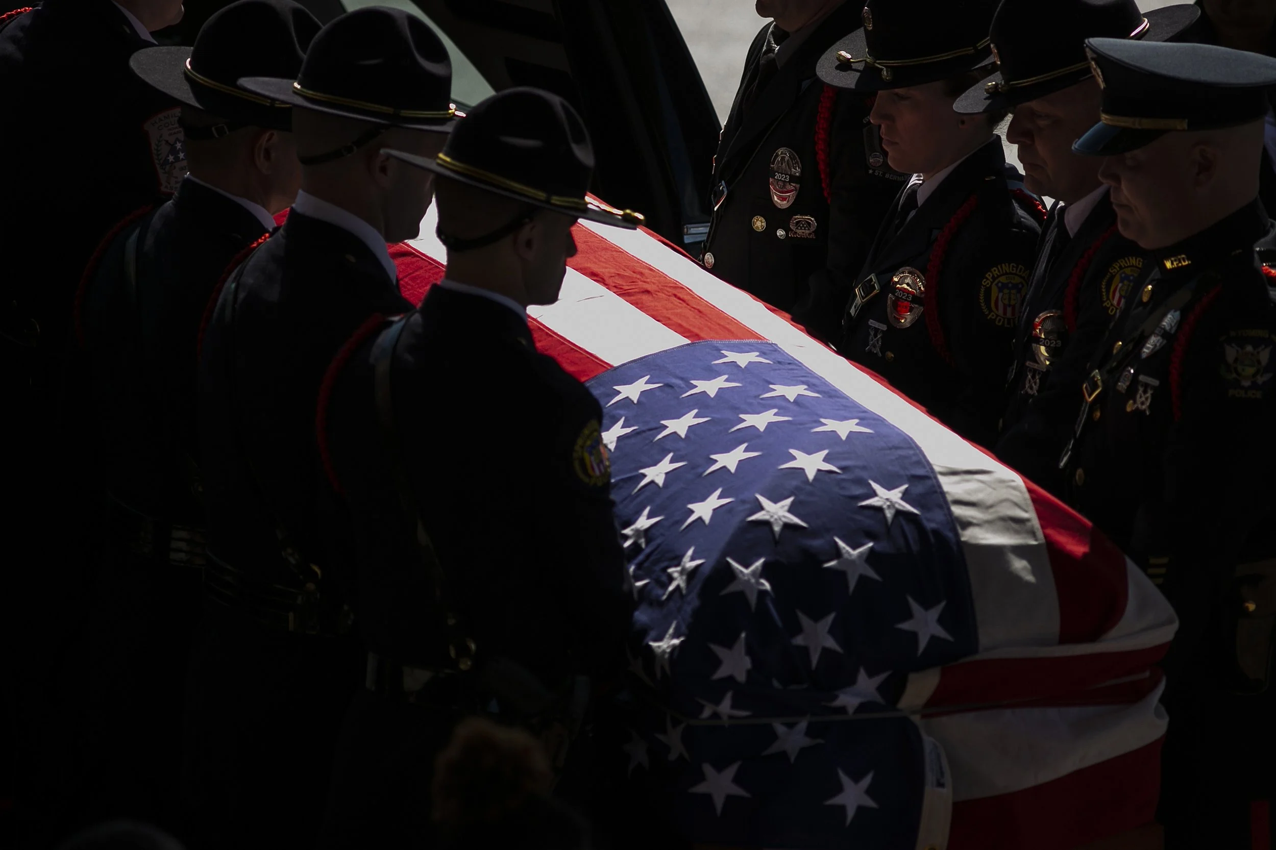 Police officers in uniform participating in a funeral service, holding a flag-draped casket, during a solemn ceremony.