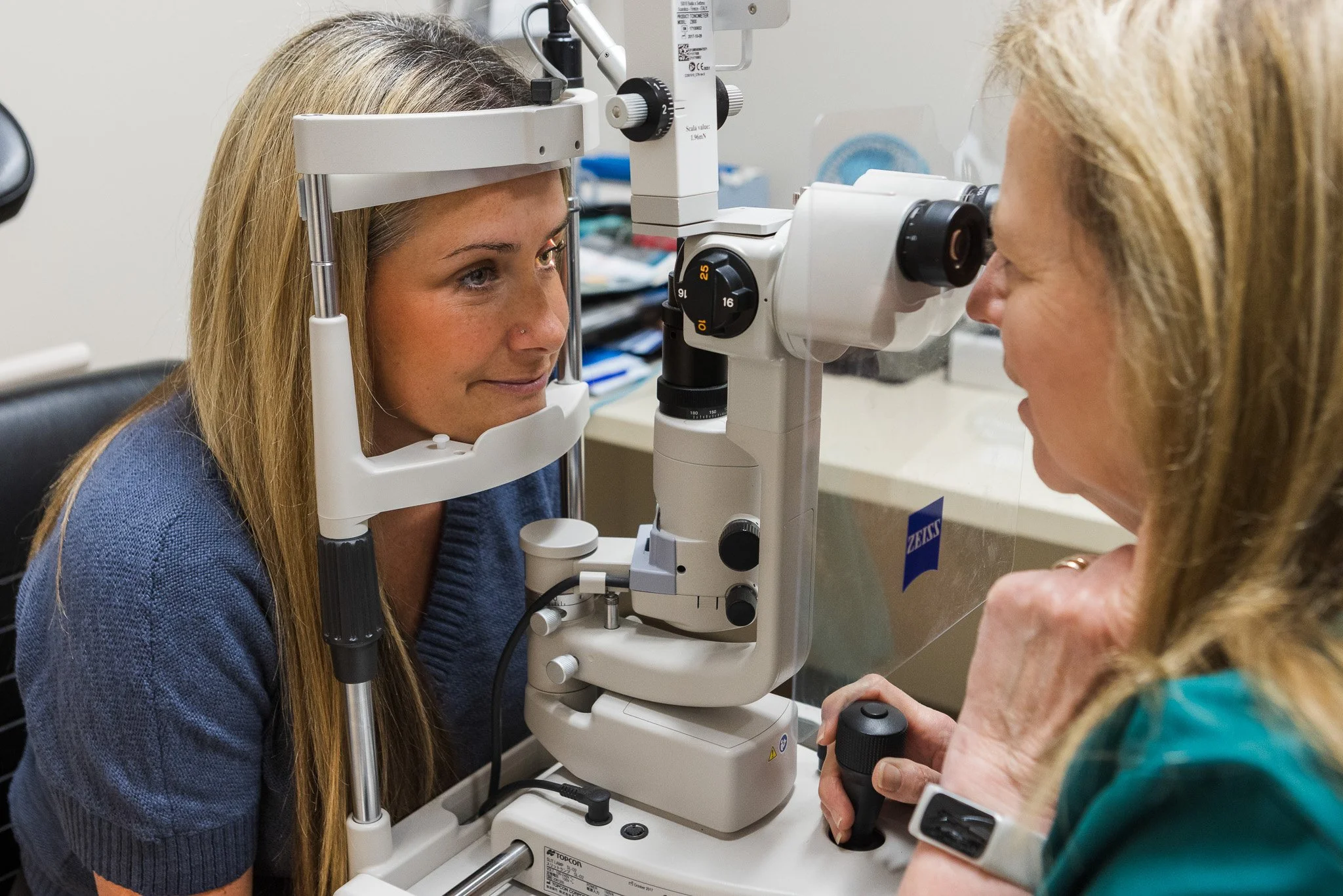 Optometrist performs eye examination on a woman using a slit lamp diagnostic device.
