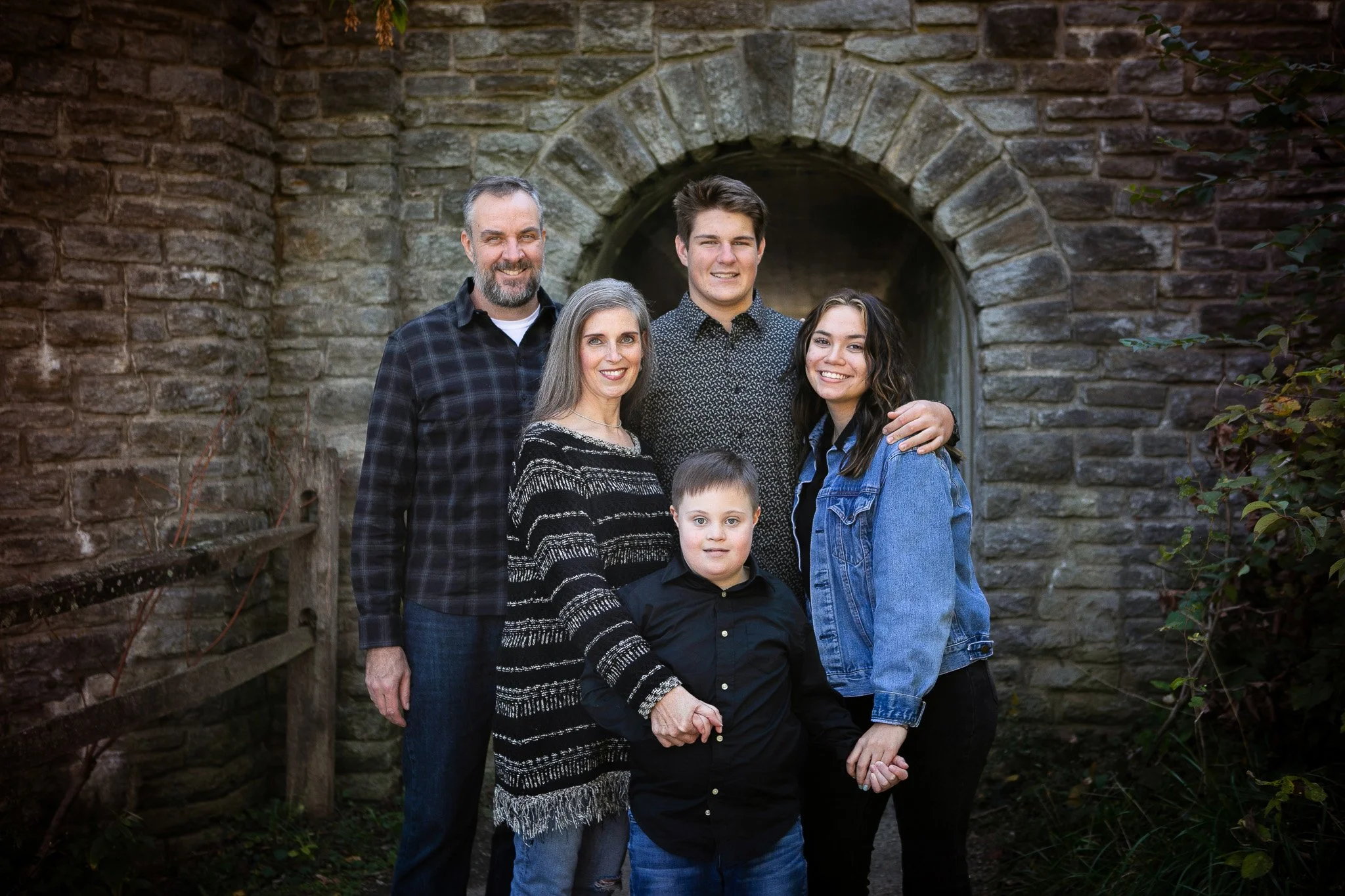 Family group standing in front of a stone archway, smiling and holding hands outdoors.