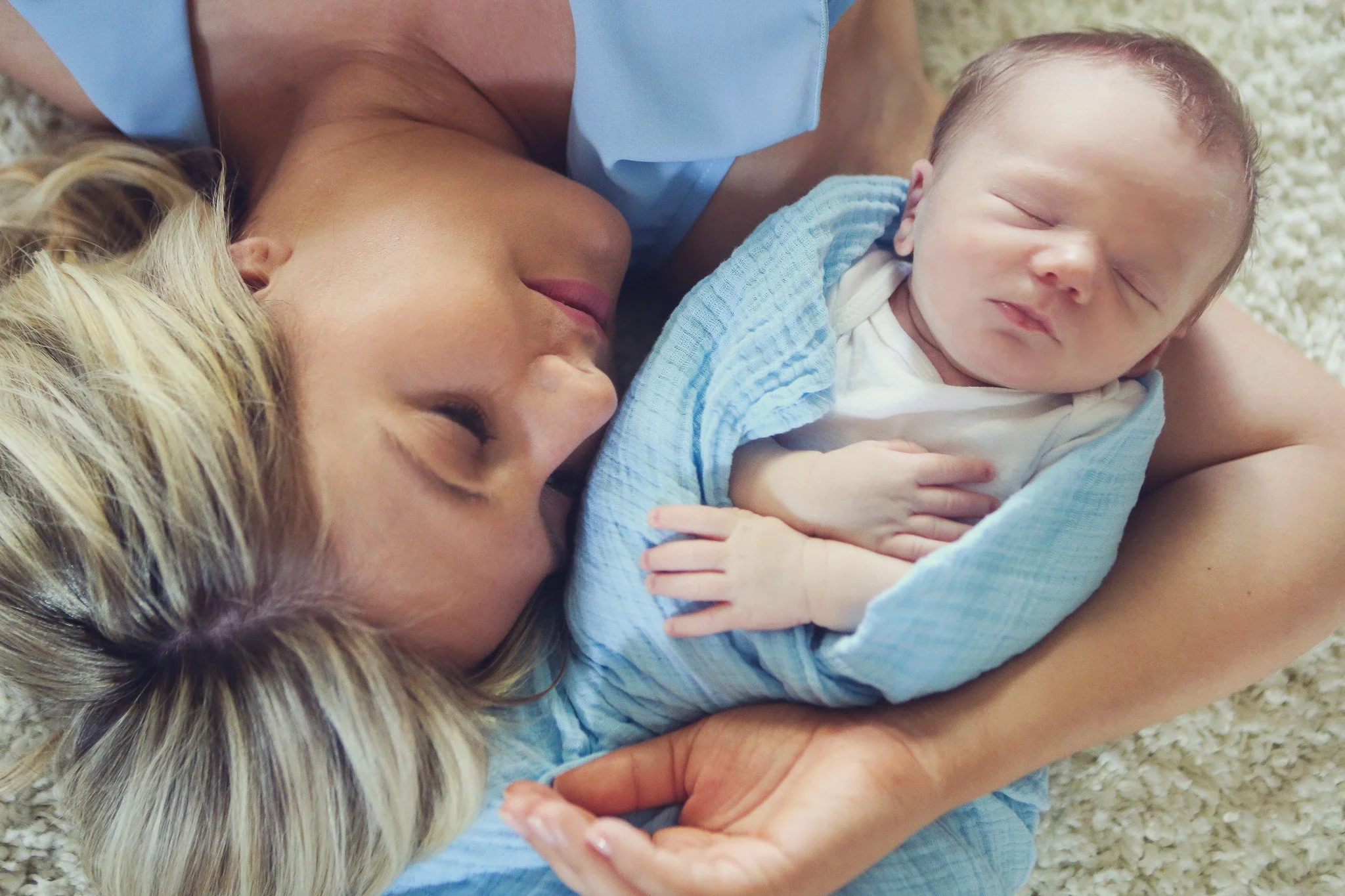A woman and a newborn baby lying on a fuzzy white rug, with the woman holding the baby and both sleeping peacefully.