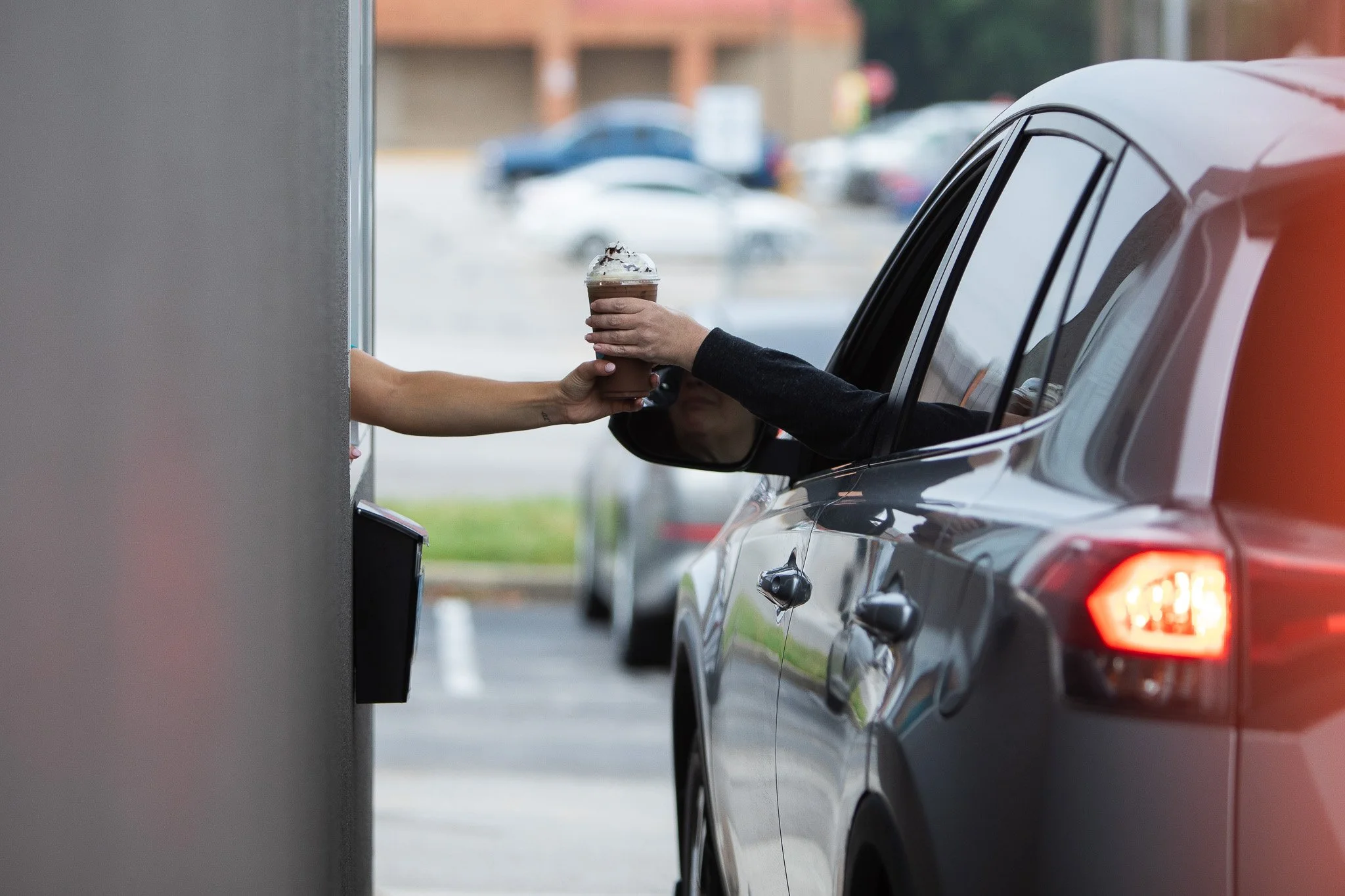 A person inside a car is receiving a coffee through the window from a Dunkin' drive-thru employee.