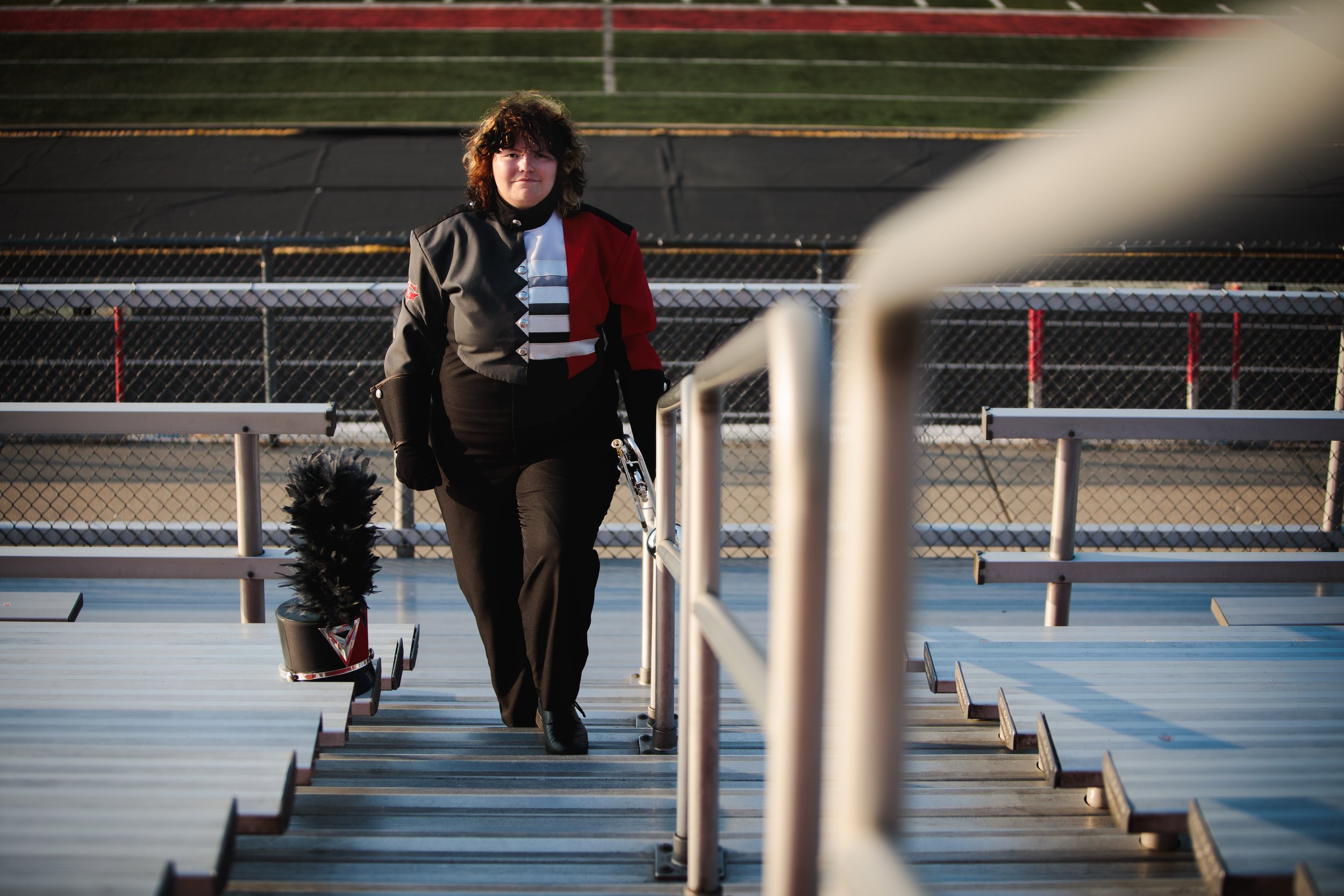 A senior dressed in a marching band uniform standing on bleachers at Goshen High School stadium, holding a trumpet.